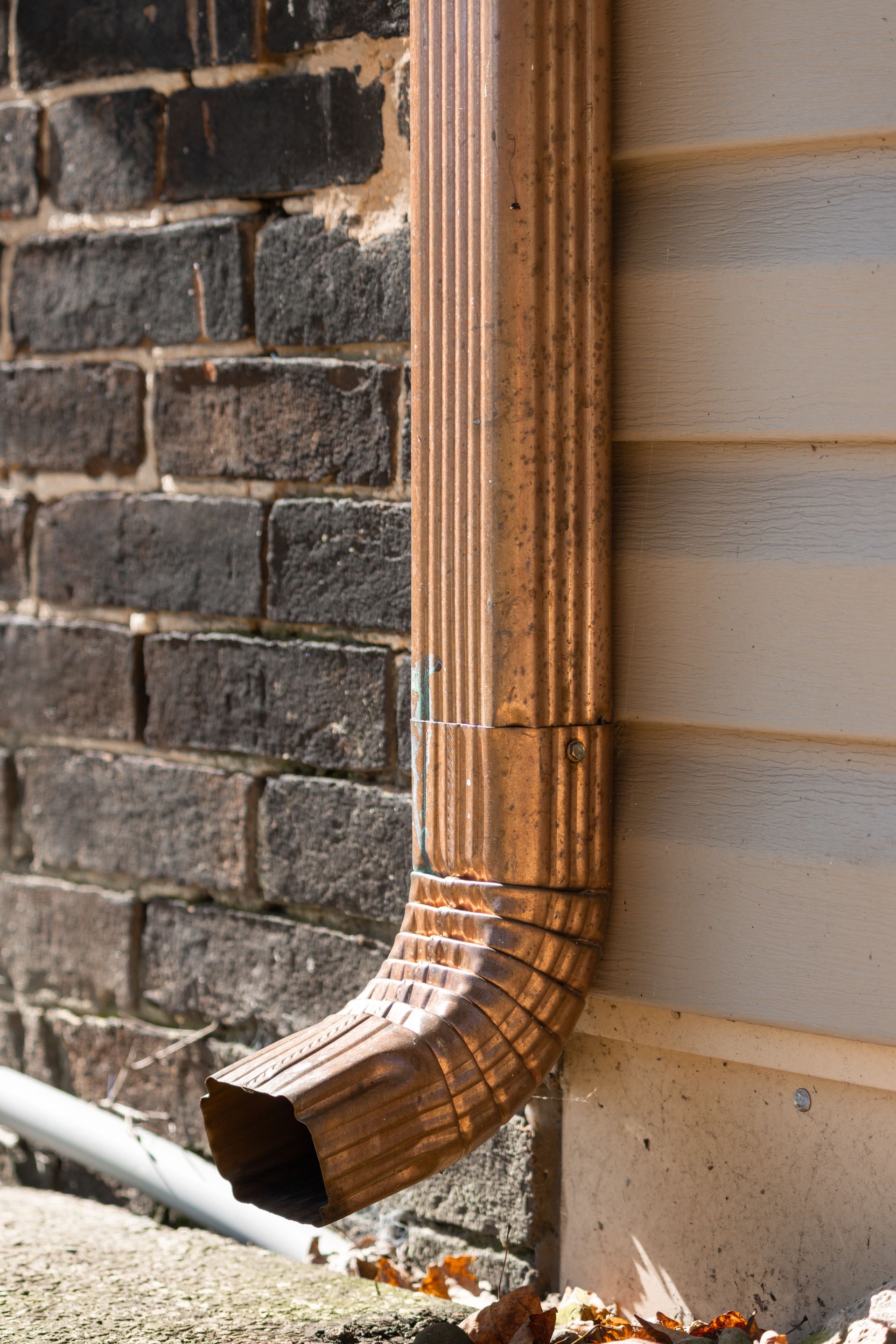 Copper downspout against a brick wall and siding.