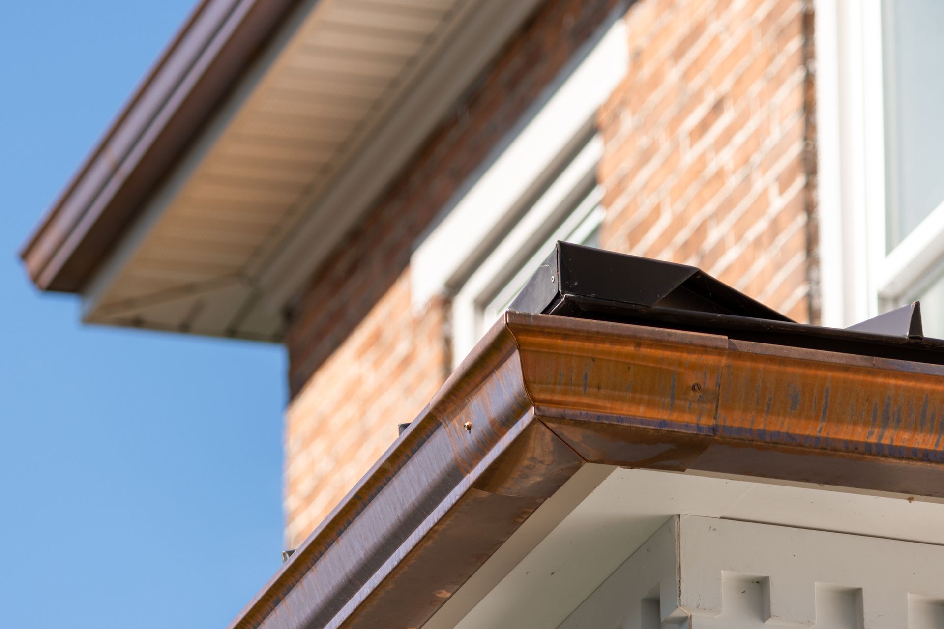 Copper-colored gutters and trim on a brick building against a blue sky.