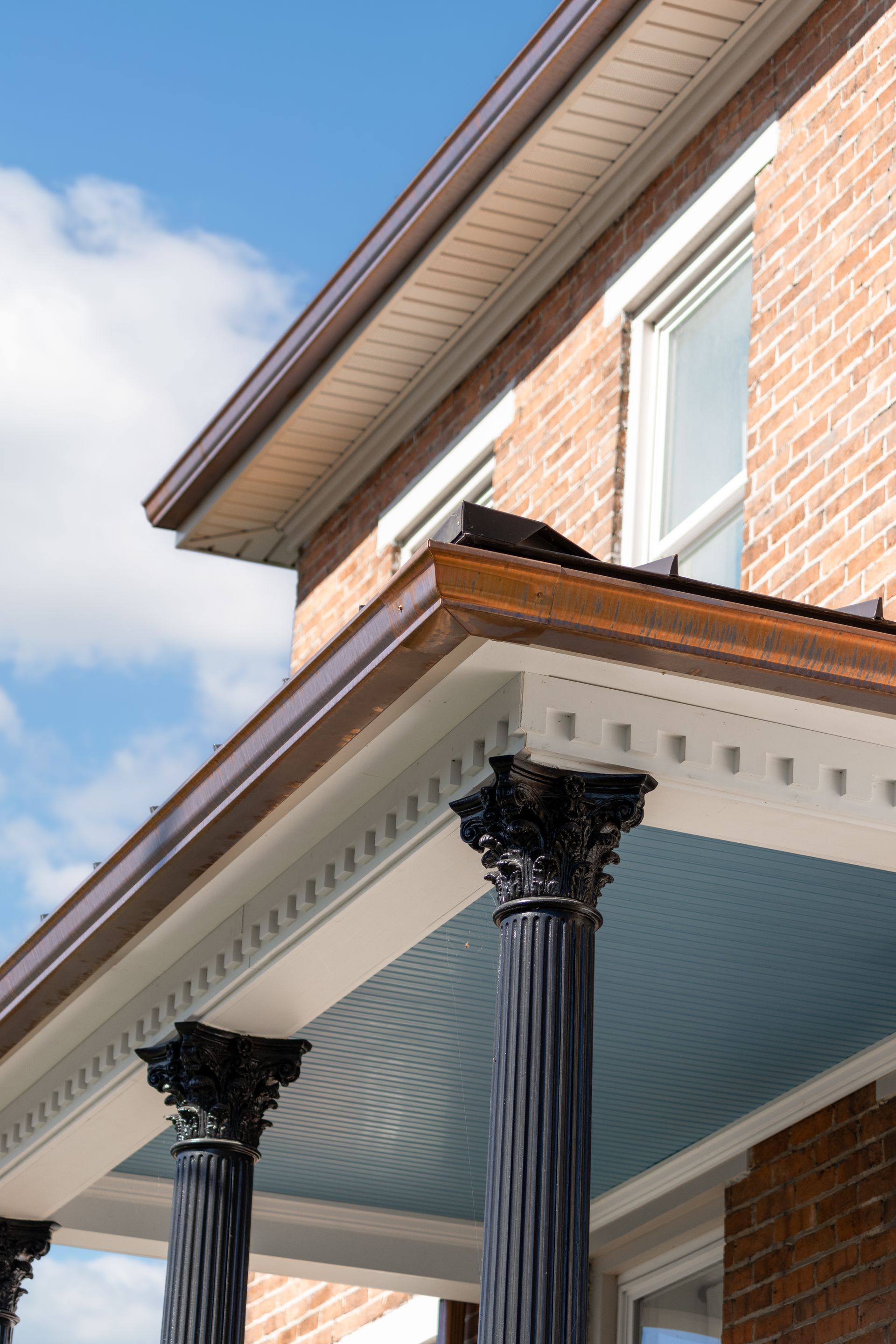 Brick building with dark columns, copper gutters, and a blue porch ceiling.