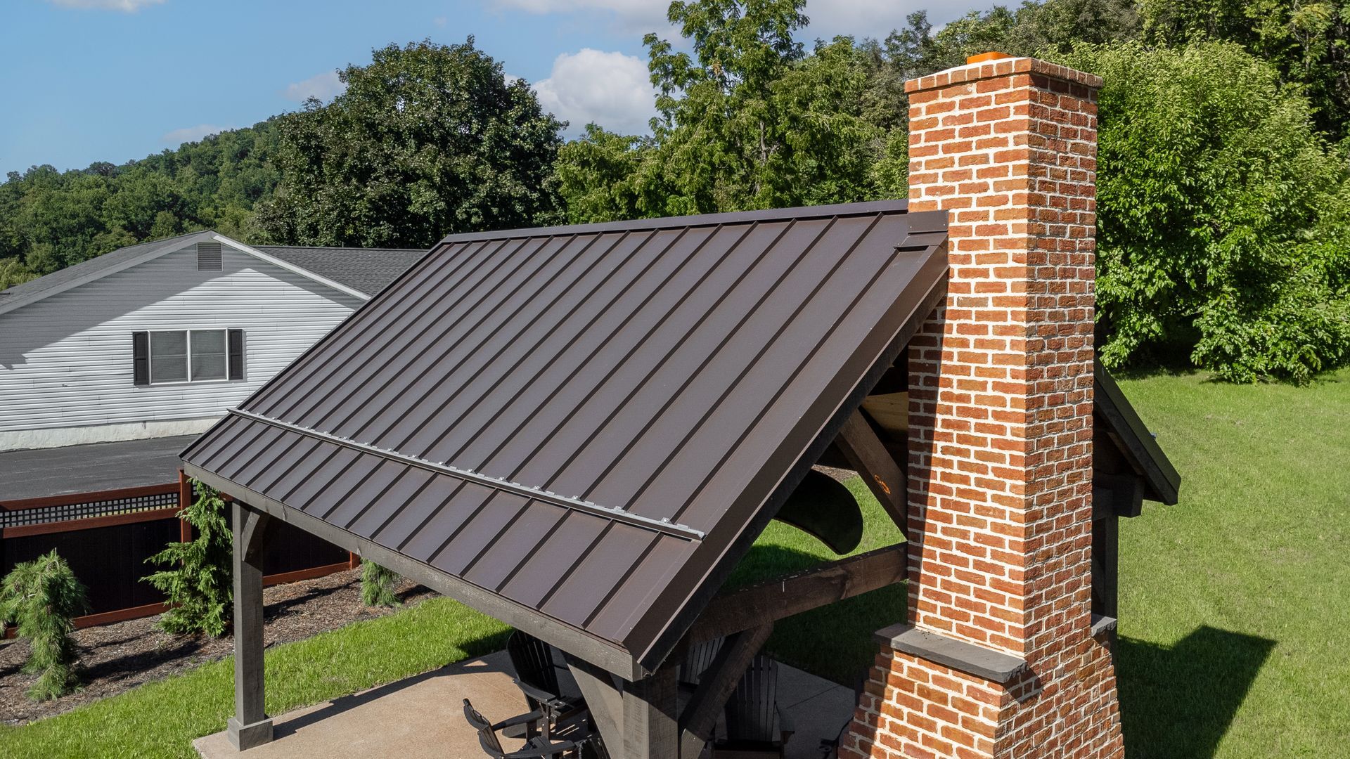 Dark brown metal roof on a wooden structure with a brick chimney in a grassy yard.