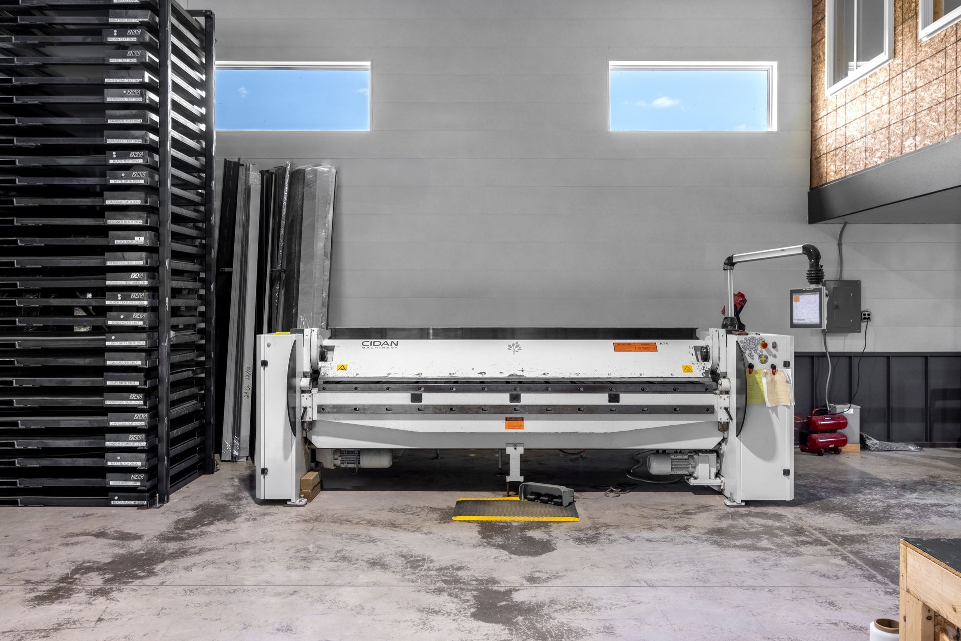 Metal bending machine in a warehouse setting with stacks of metal sheets.