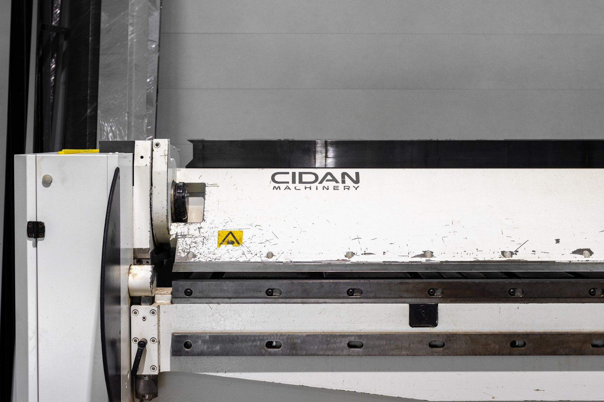White Cidan machine with a yellow caution sign, used for metal fabrication in a workshop.