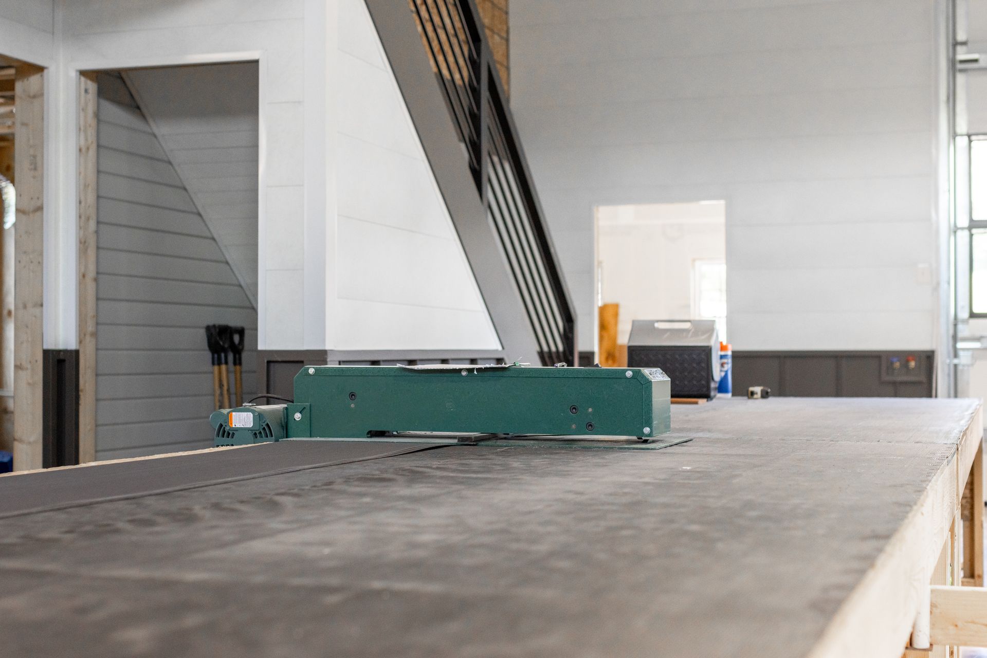 Green industrial machine on a gray surface in a modern building, stairs visible in background.