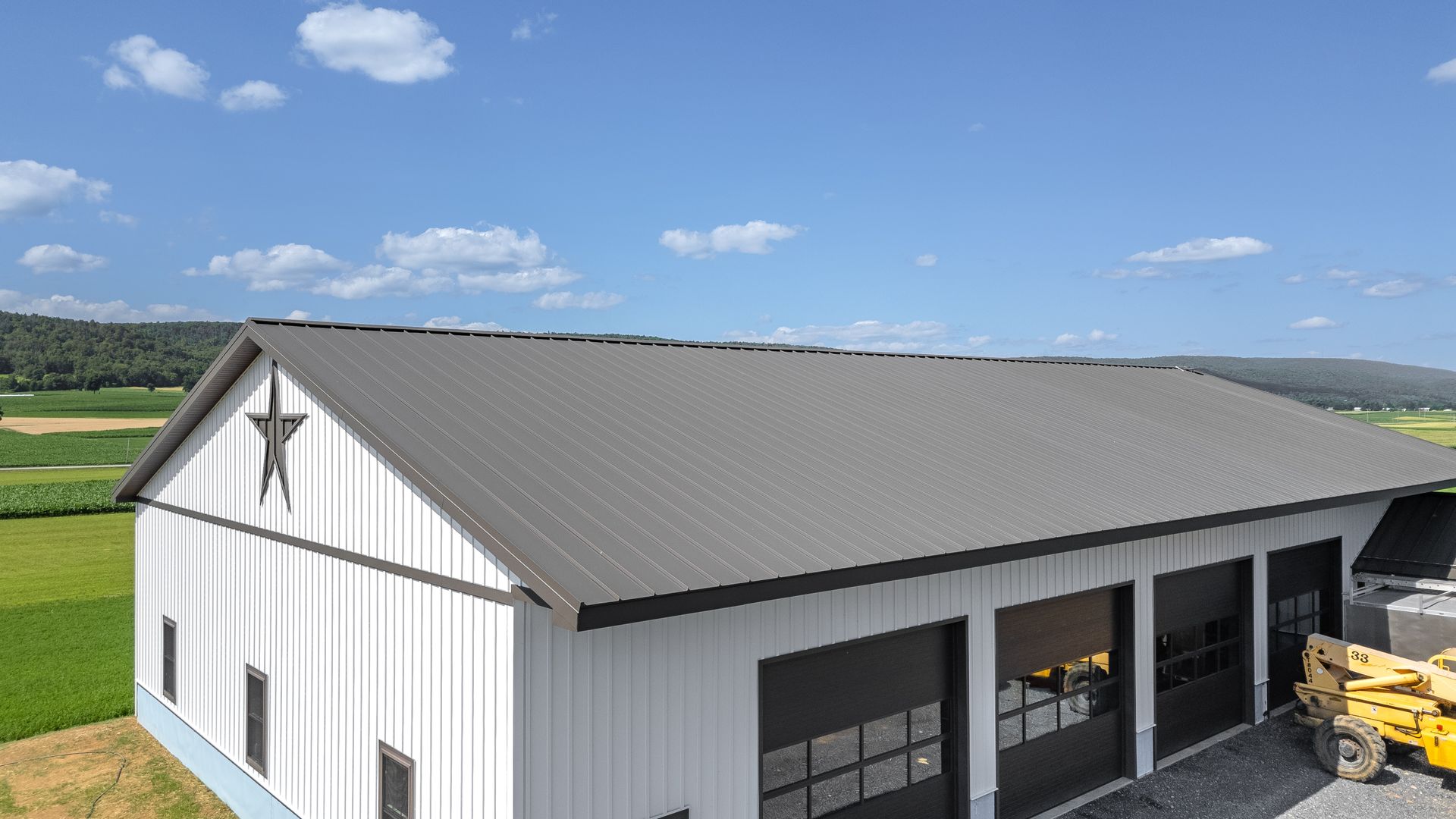 White barn with dark gray roof and garage doors, star emblem, sunny outdoor setting.
