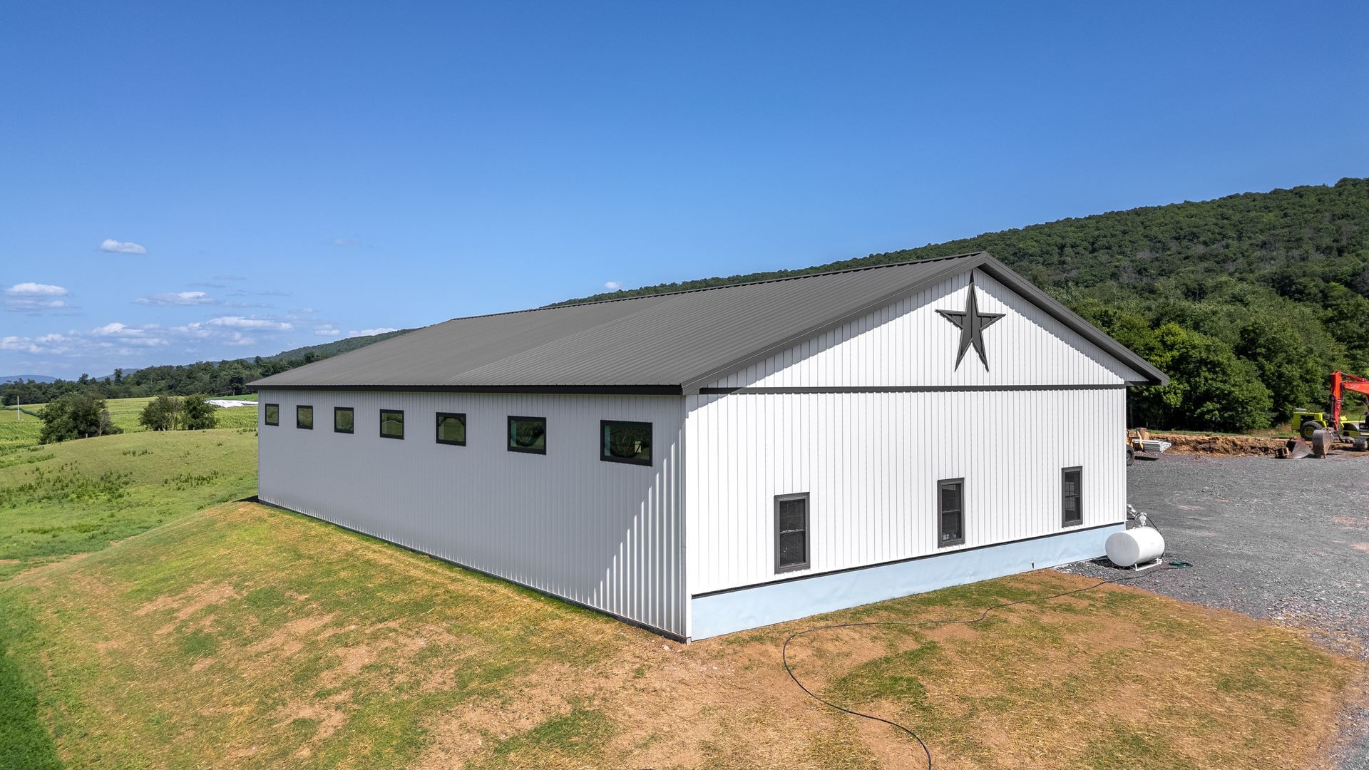 White barn with dark grey roof, black windows, and star emblem on the side, set in a rural landscape.