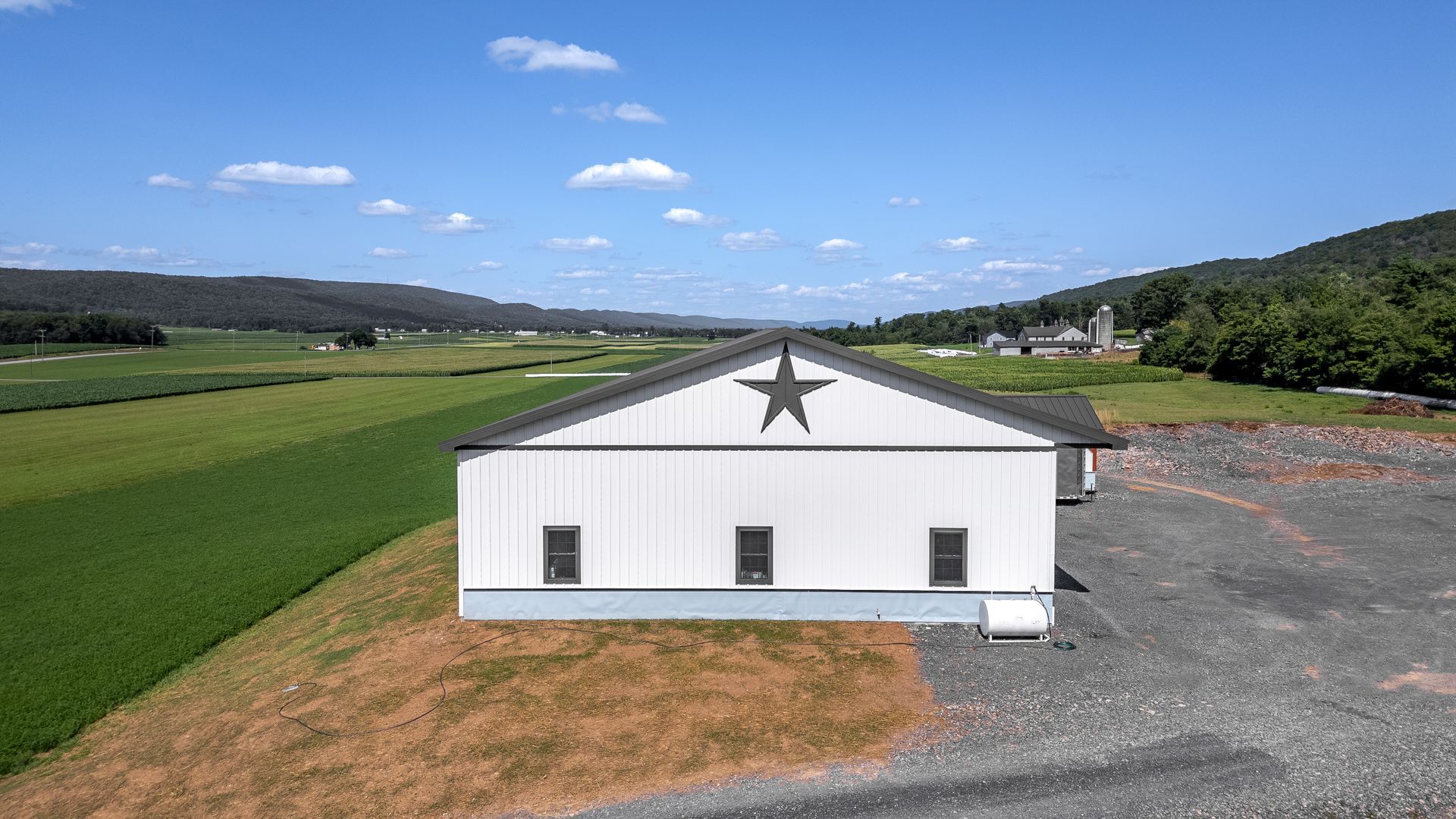 White barn with black star on roof; in a field with mountains in the background.