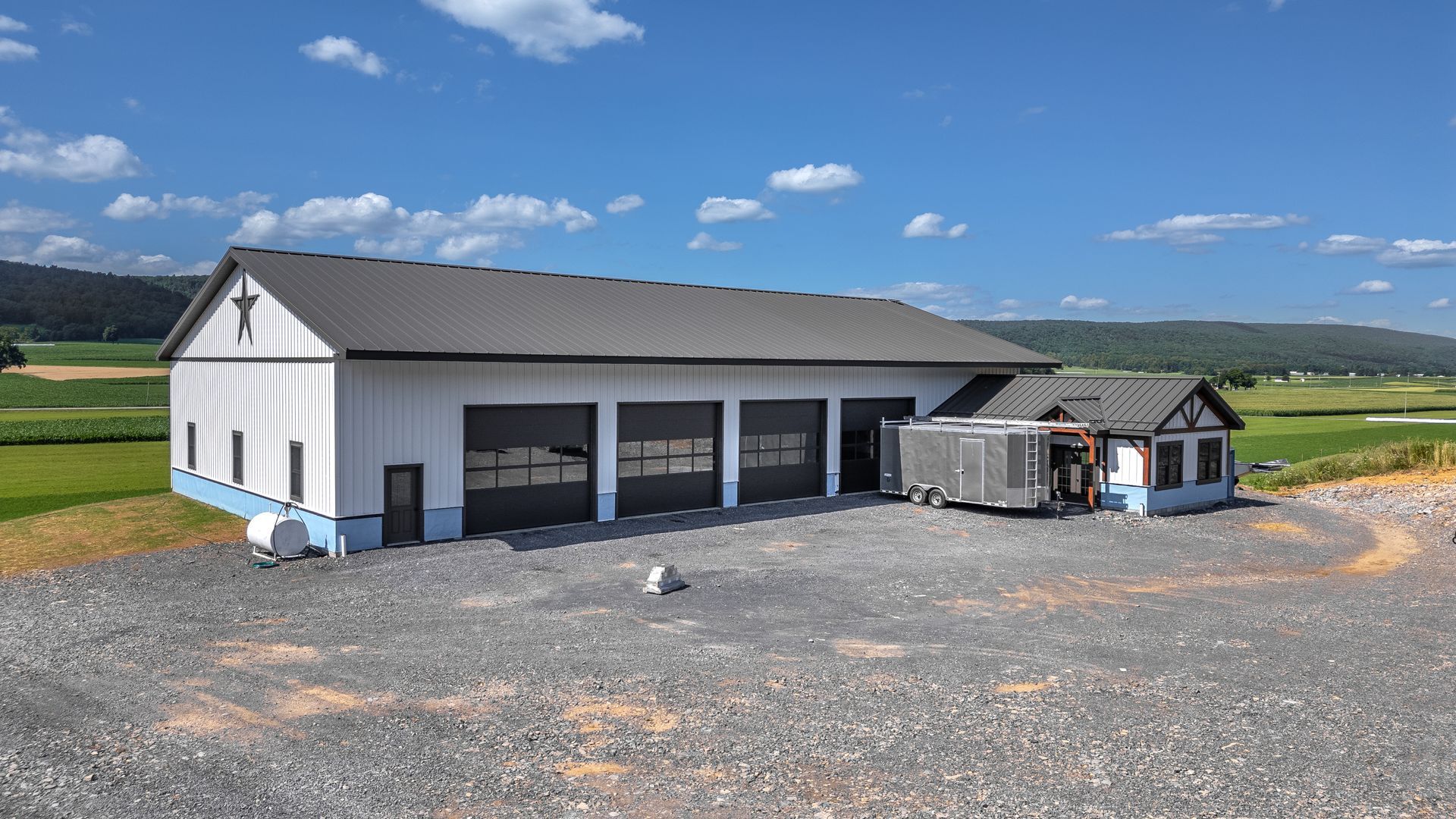 White and gray garage with four bays, small adjoining structure, and gravel driveway under blue sky.