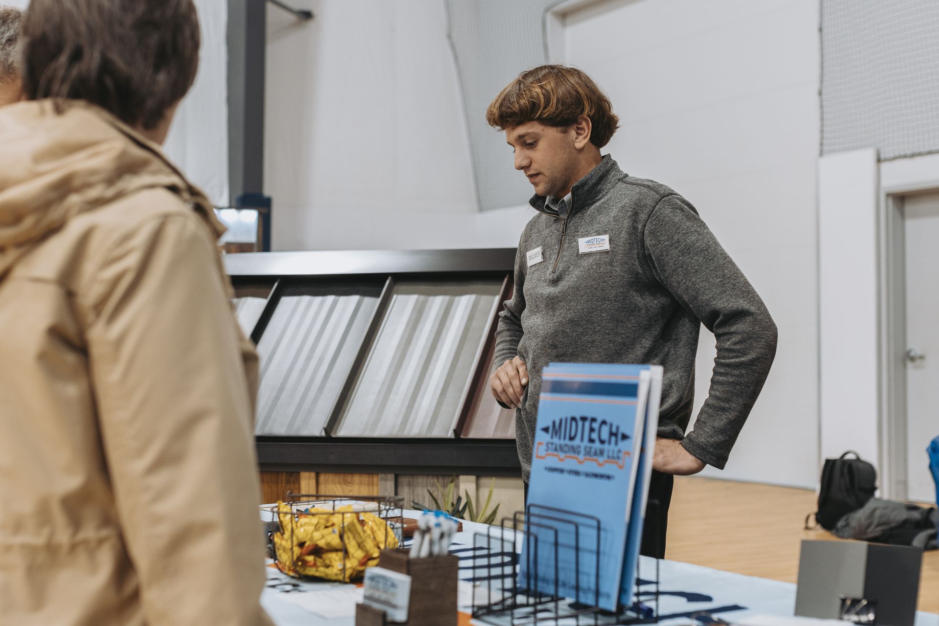 Man at a trade show booth, gesturing towards displays of materials, speaking to a customer.