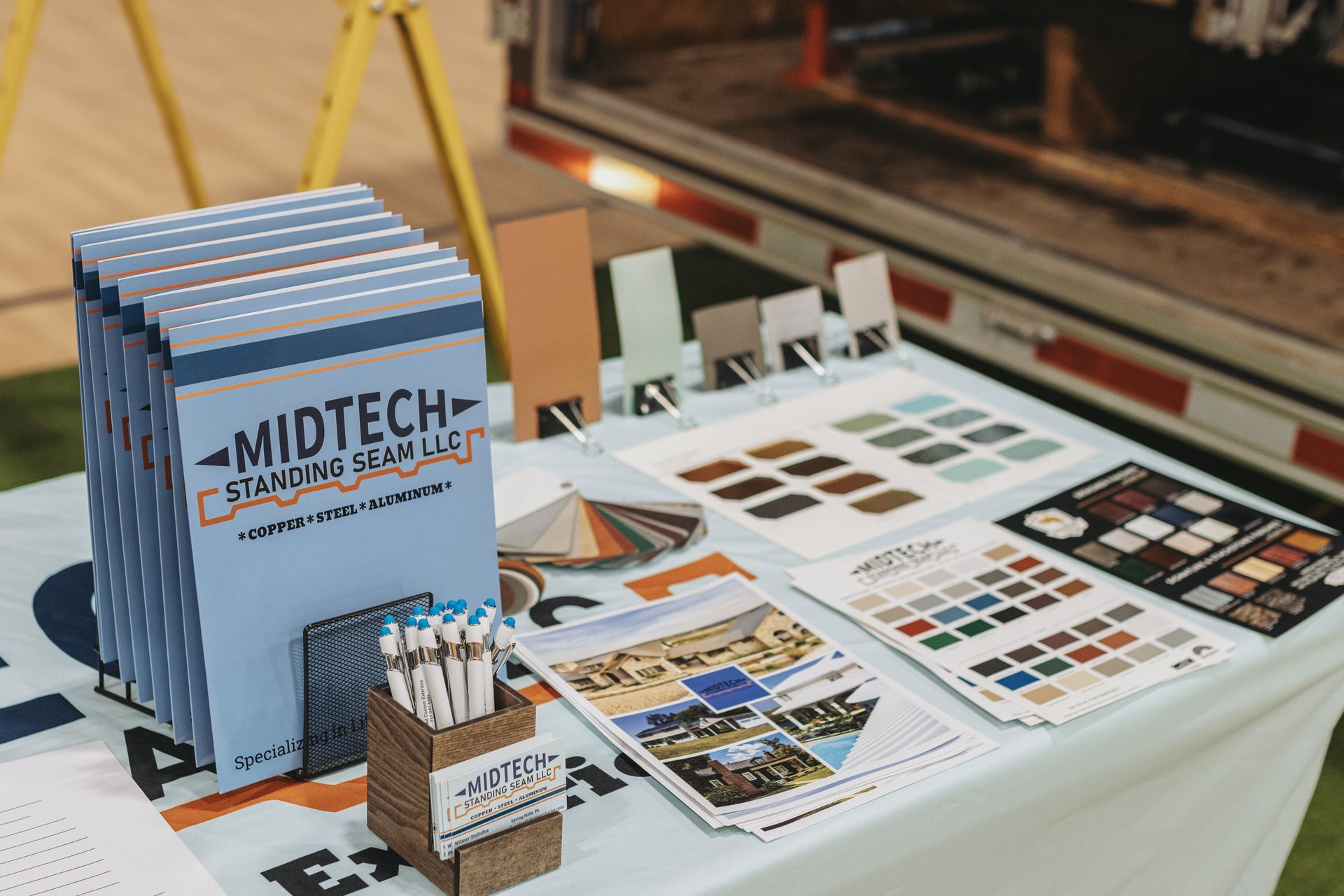 Table with brochures and samples for Midtech, possibly at a tradeshow, with light blue and orange branding.