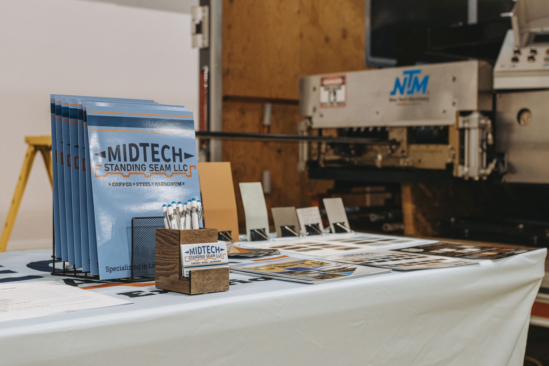 Table display with Midtech Manufacturing LLC materials and industrial machine in the background.