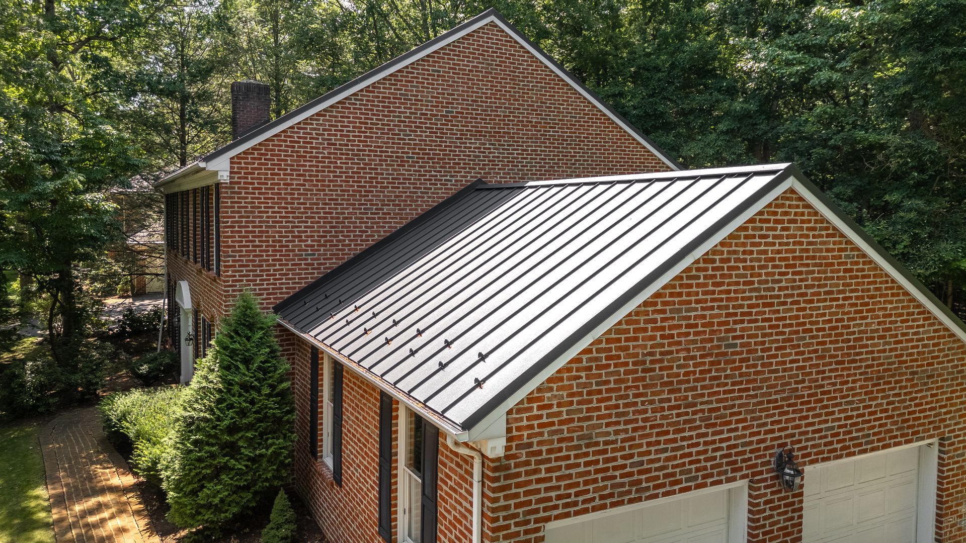 Brick house with black metal roof, surrounded by trees.