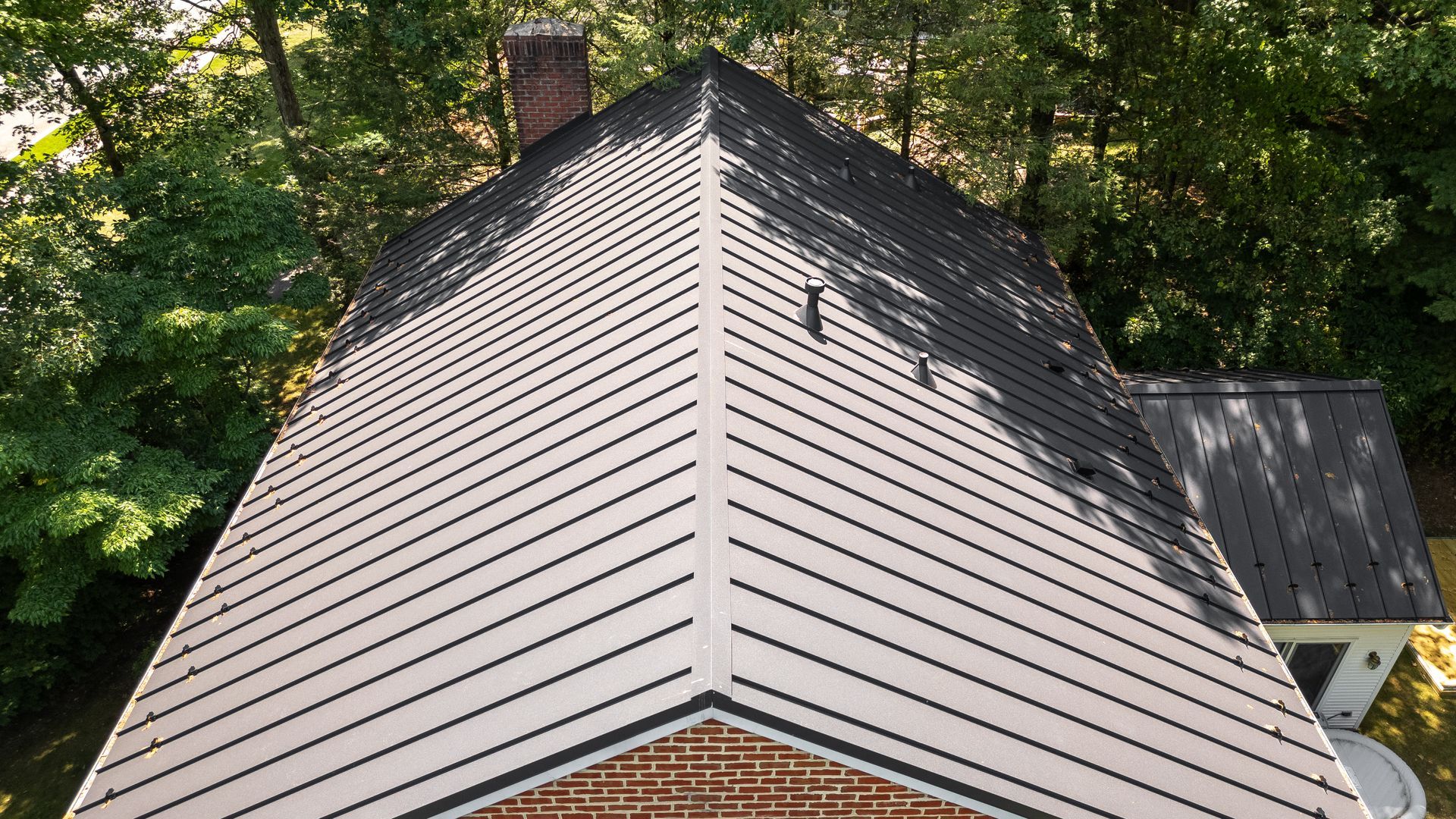 Overhead view of a house with a light roof, dark vertical lines, and a brick chimney.