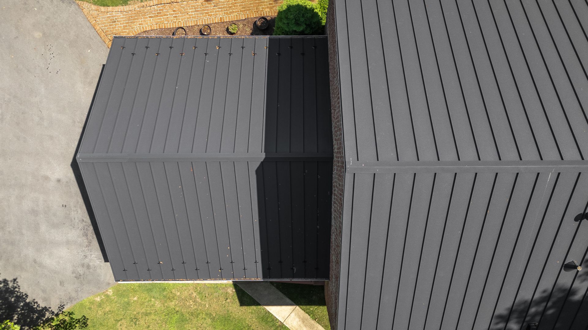 Overhead view of a house with a dark gray corrugated metal roof and asphalt driveway.