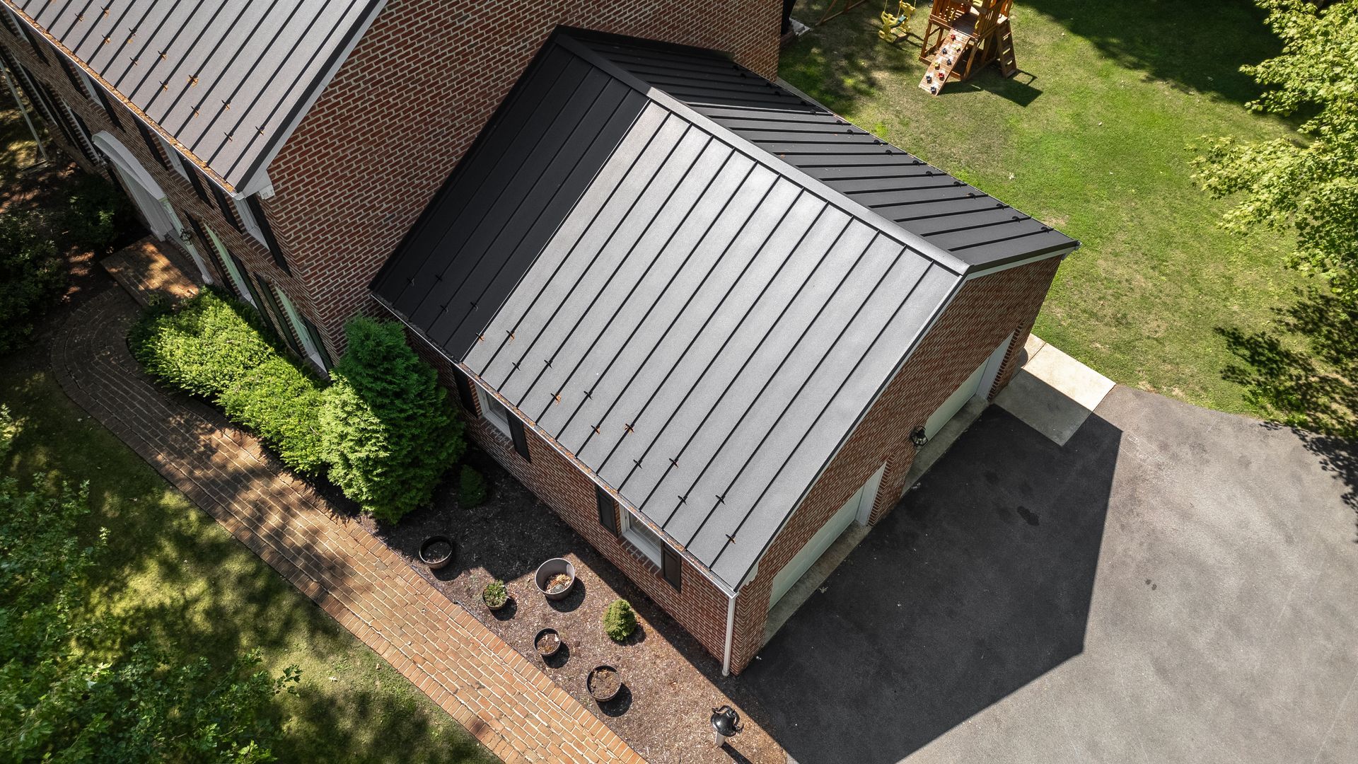 Brick house with a black metal roof, driveway, and green lawn.