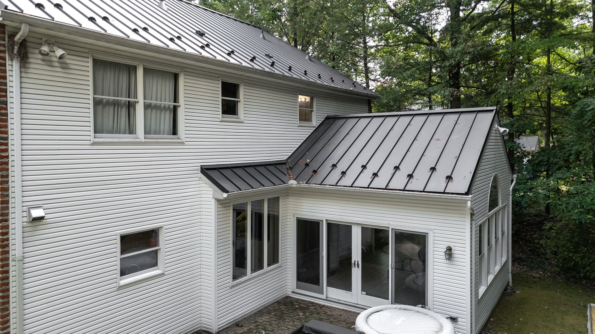 White house with a dark gray metal roof and an attached screened-in porch, surrounded by trees.