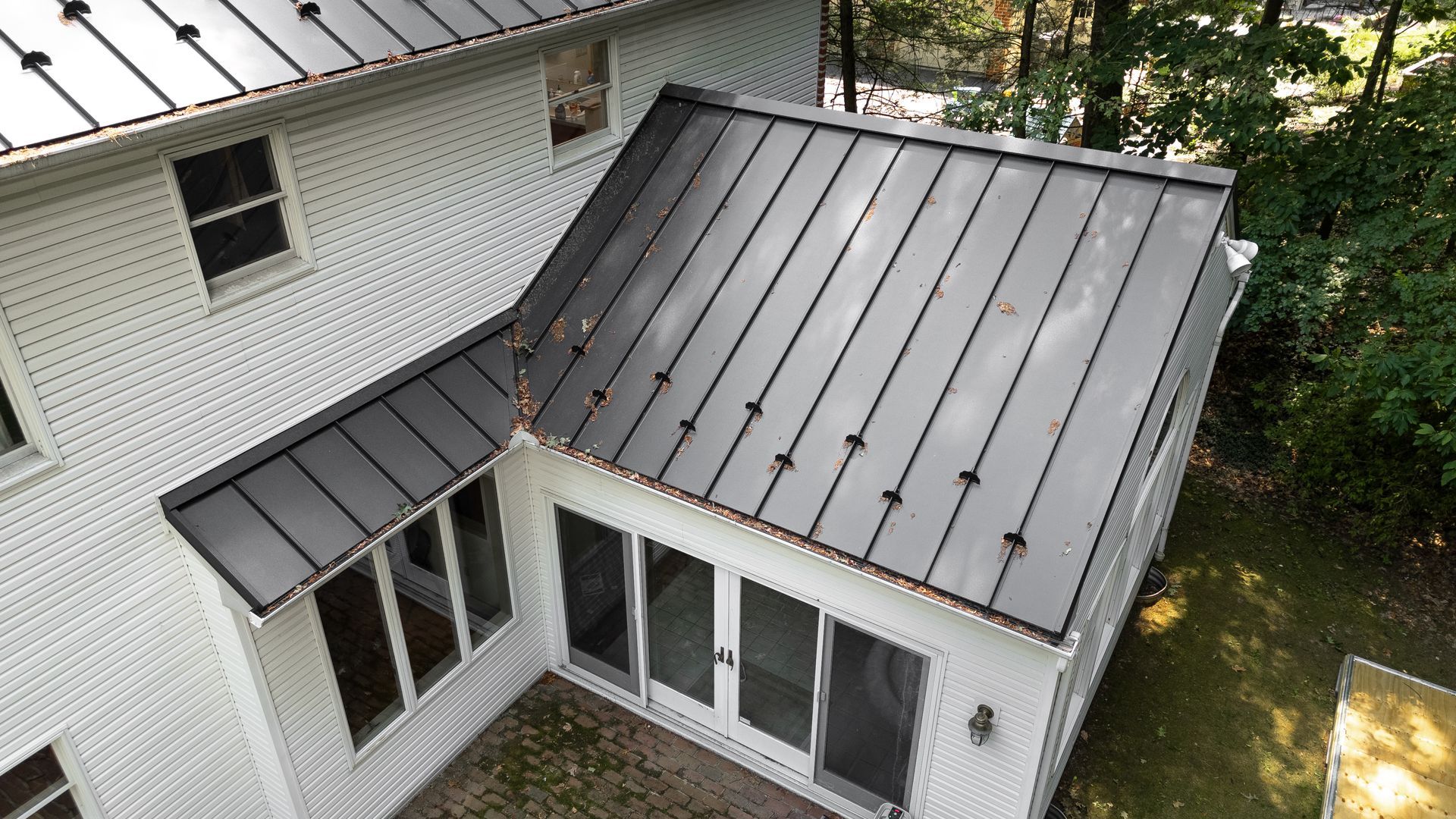 White house with black metal roof and glass doors, surrounded by trees.