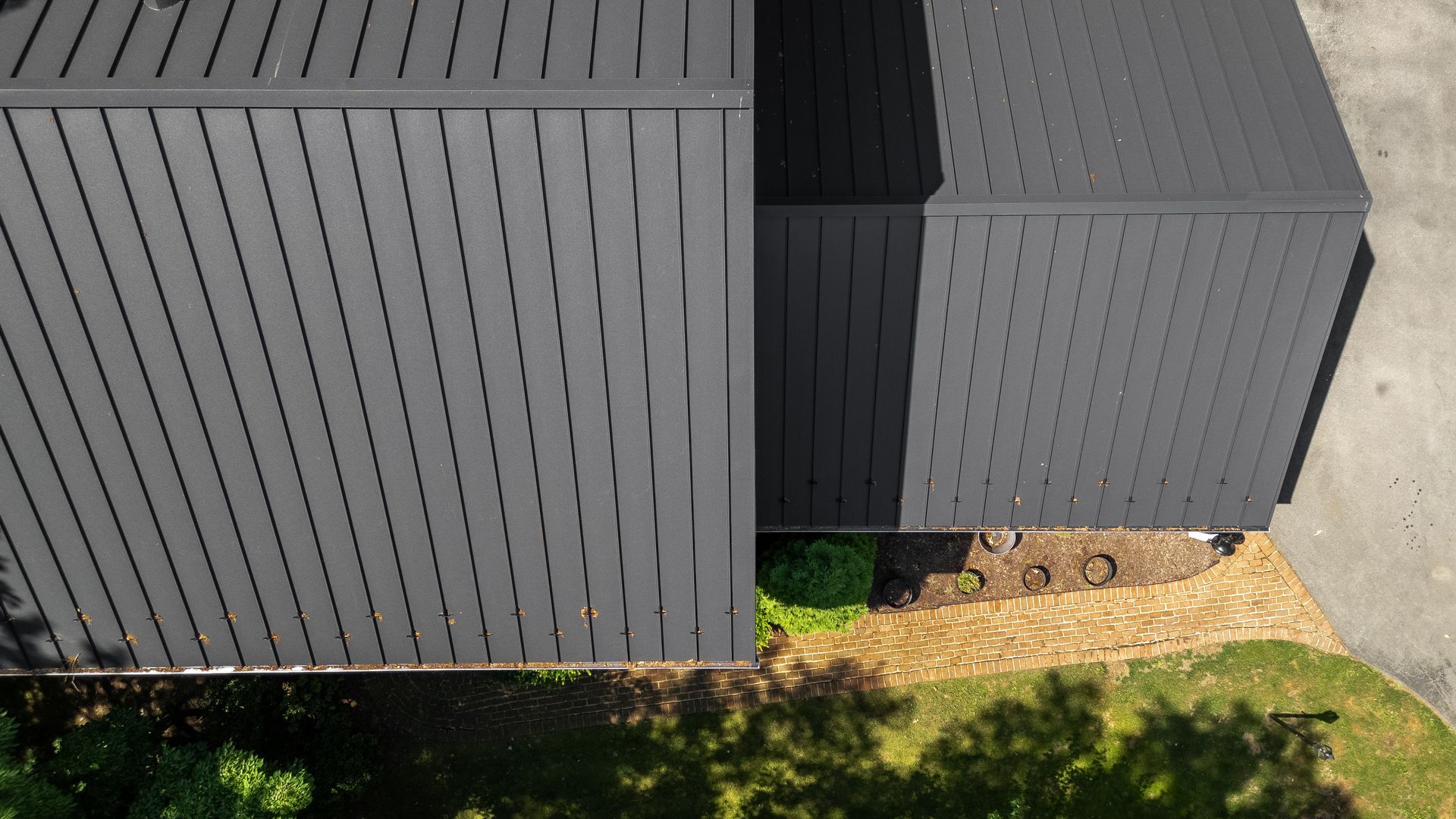 Overhead view of a dark gray metal roof on a house. Green grass and a walkway are in the foreground.