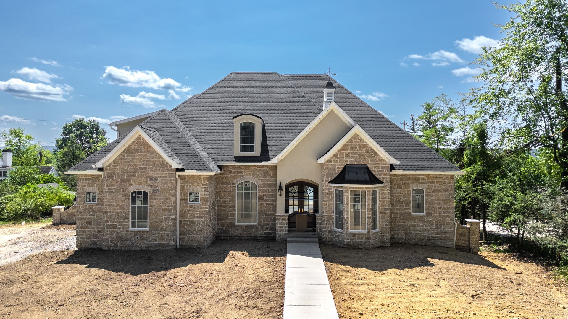 Stone house with gray roof, arched windows, and a concrete walkway on a sunny day.