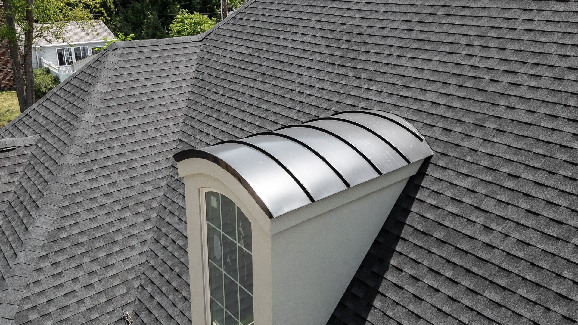Dormer with arched, metal roof on a dark gray shingle roof.