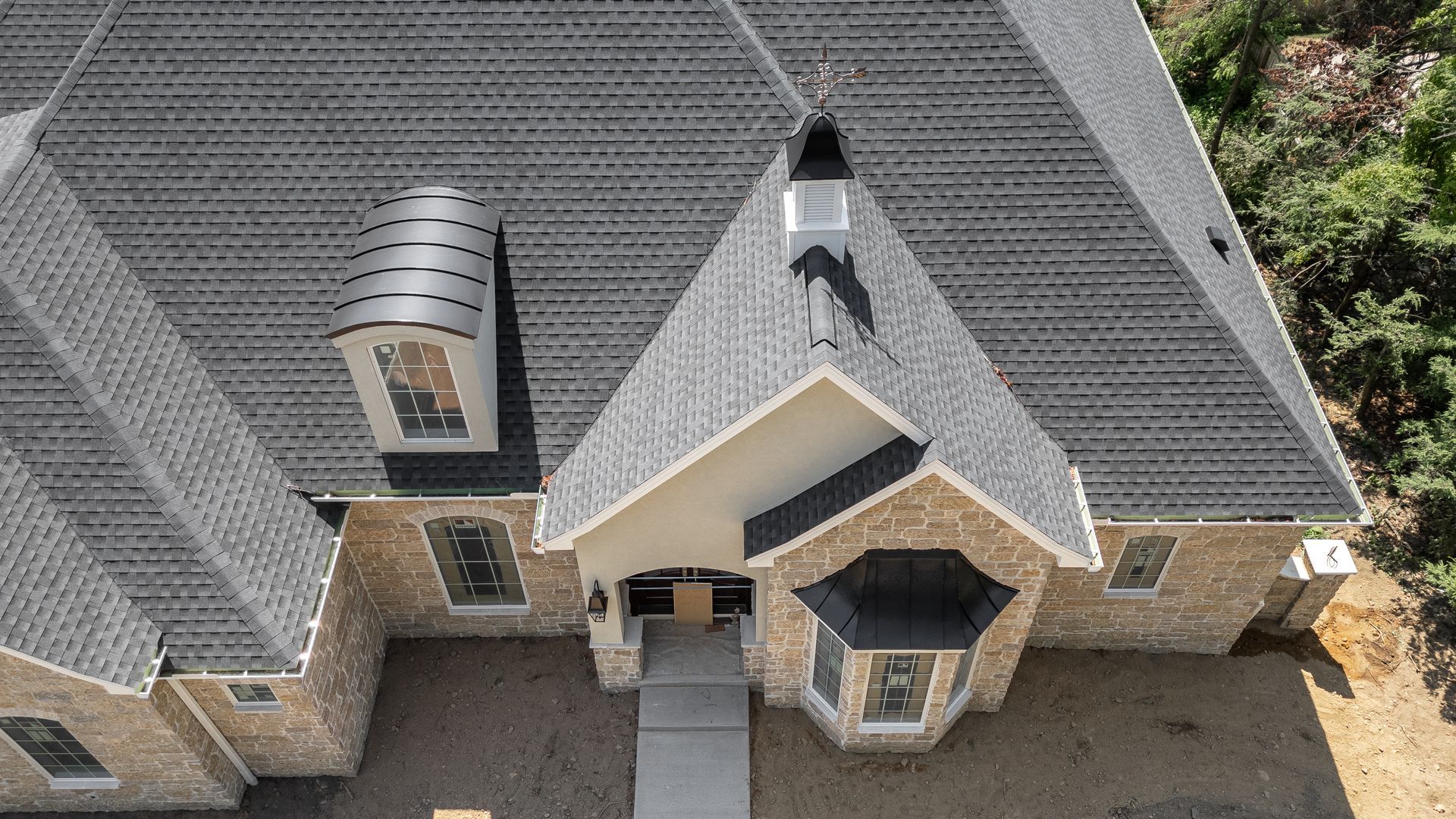 Overhead view of a house with gray roof and stone exterior. Entryway has a concrete path.