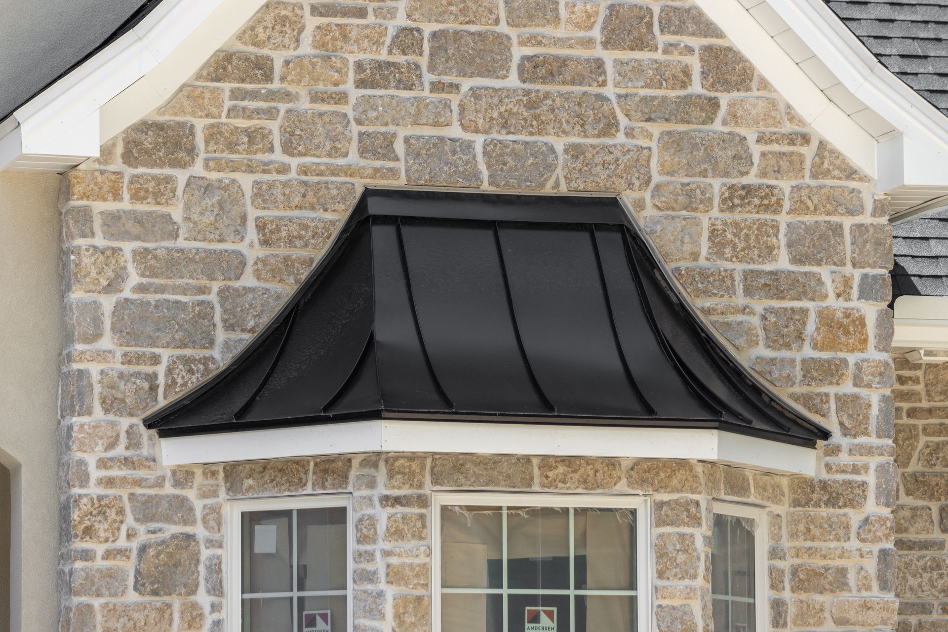 Black metal awning above a bay window on a stone facade.