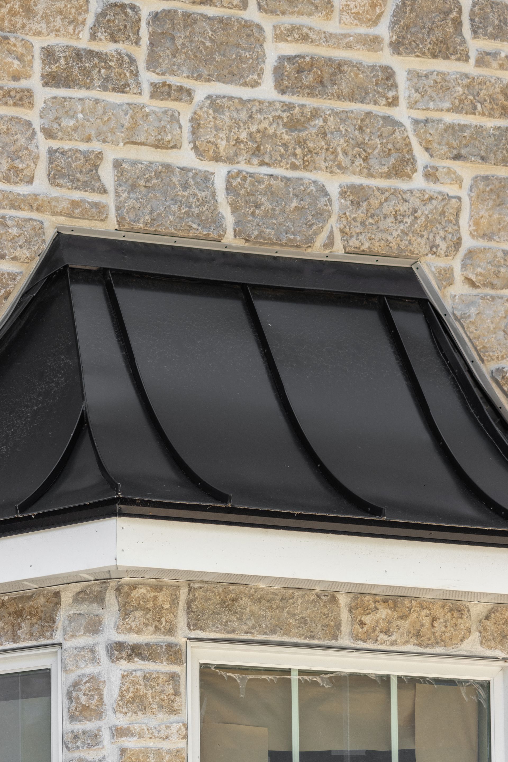 Black metal roof over a window bay with light stone walls.
