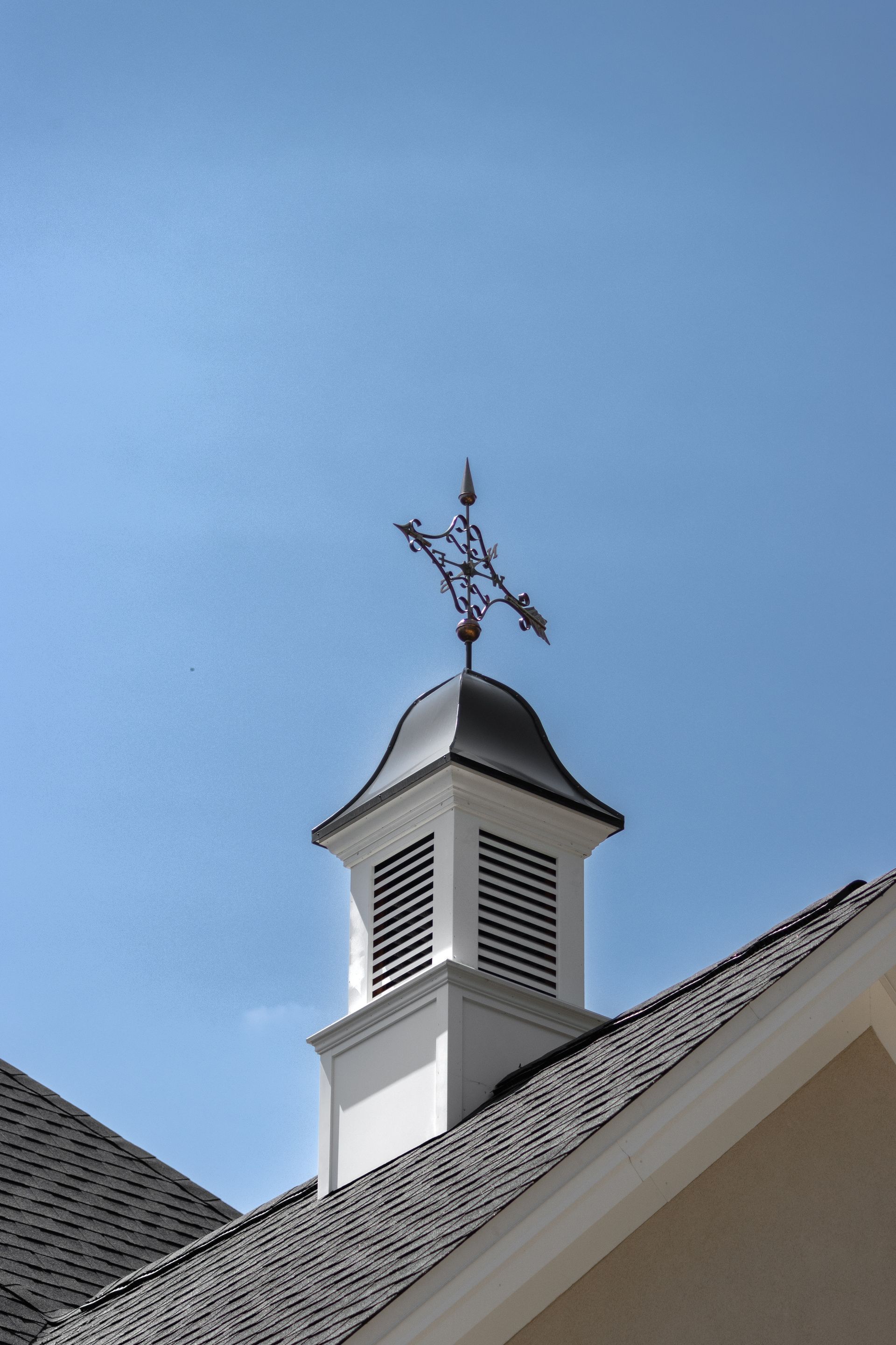 White steeple with a black dome and weather vane against a blue sky.
