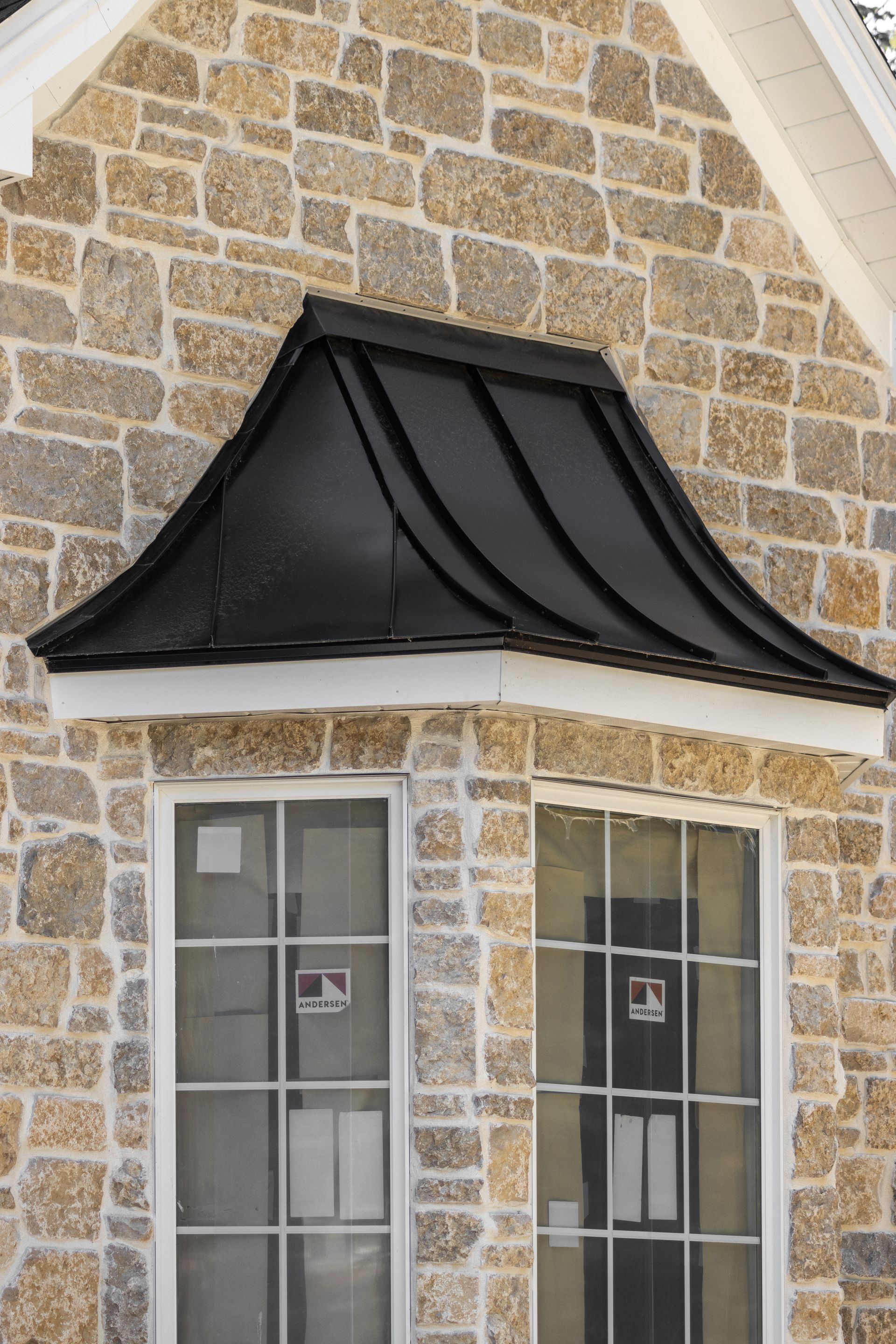 Black metal roof above two windows in a stone building.