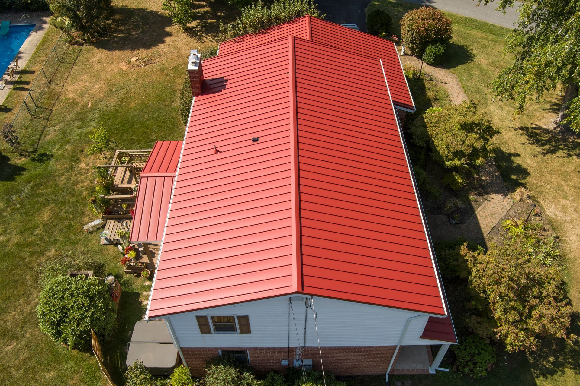 Aerial view of a house with a vibrant, modern red metal roof featuring a unique circular pattern design.