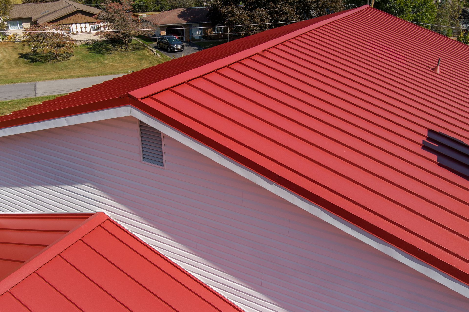 An aerial view of a bright red metal roof on a suburban home, showing the gabled structure and white siding.