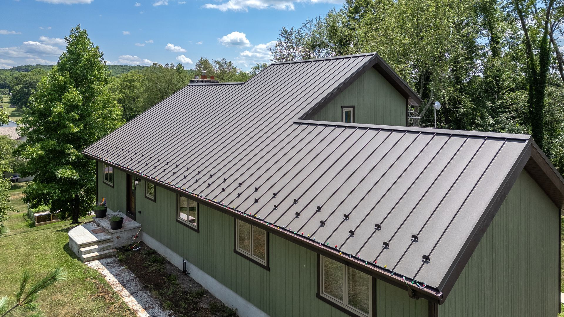 Green house with brown metal roof on a sunny day, set amongst trees.