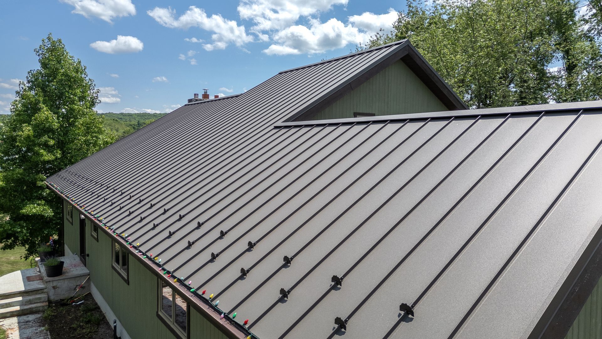 Green house with dark gray metal roof, on a sunny day.