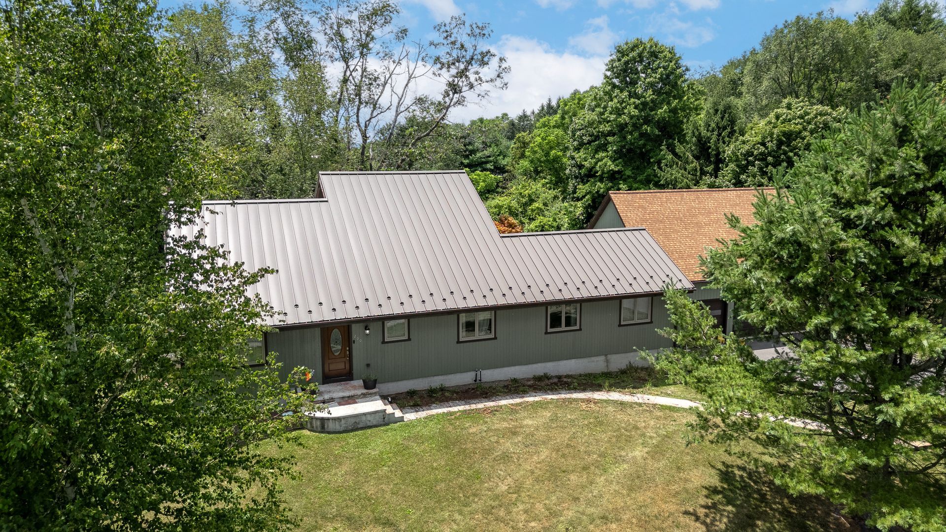Green house with metal roof, surrounded by trees and a grassy lawn.