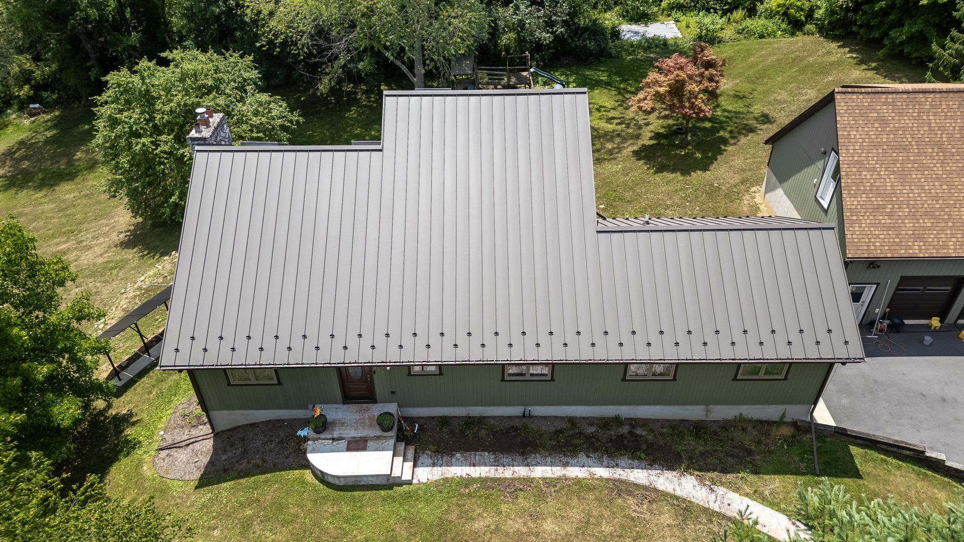 Green house with silver metal roof, surrounded by green grass and trees.