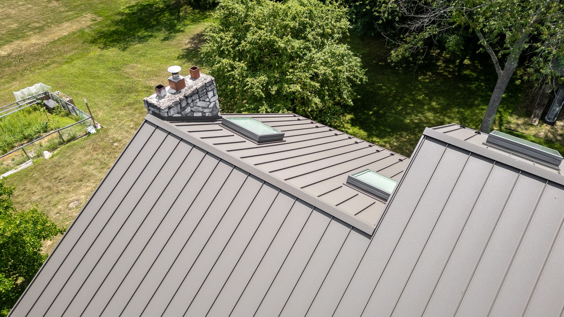 Gray metal roof with skylights and chimney in a sunny outdoor setting.