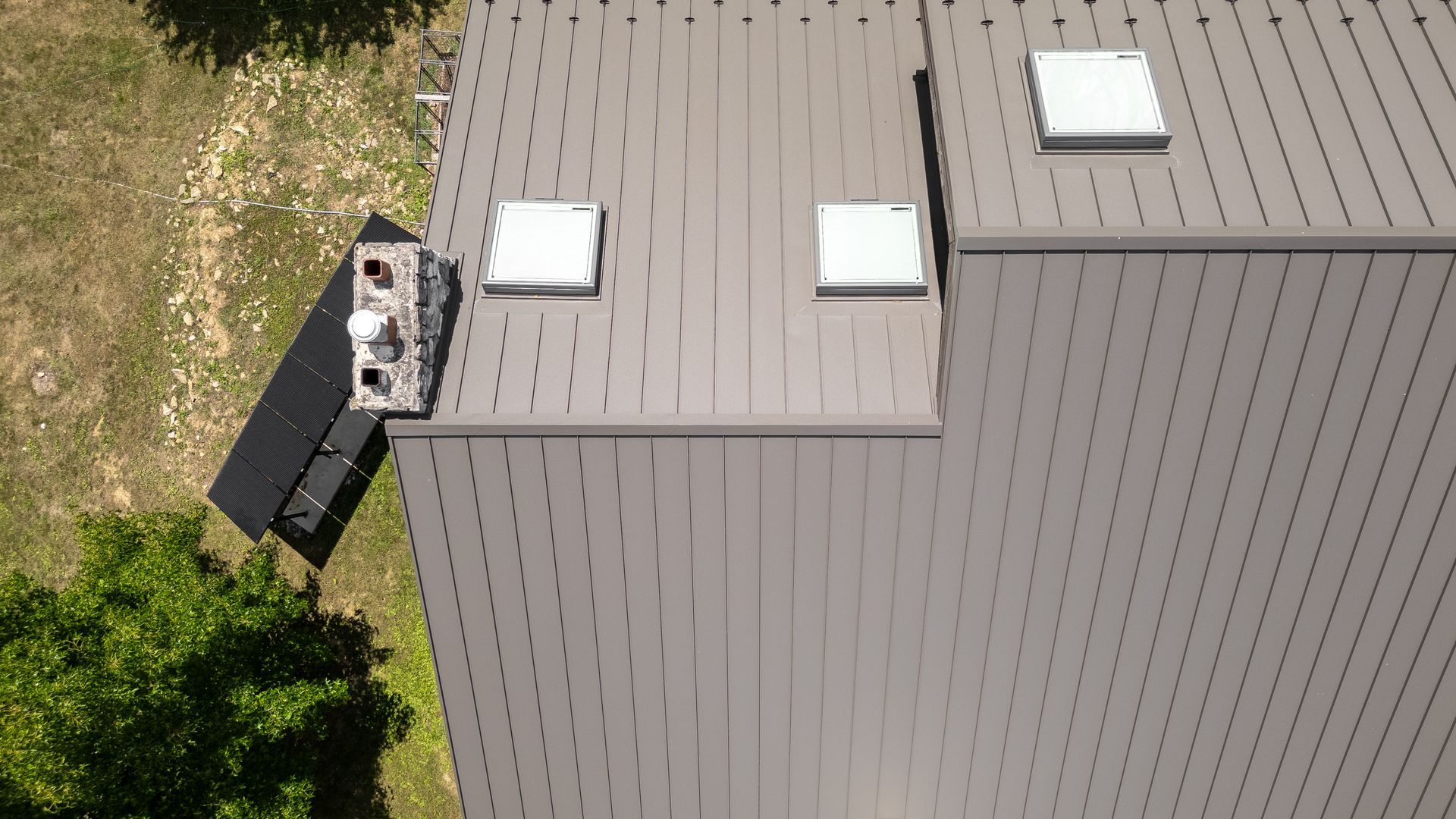 Aerial view of a gray metal roof with three skylights and a chimney.