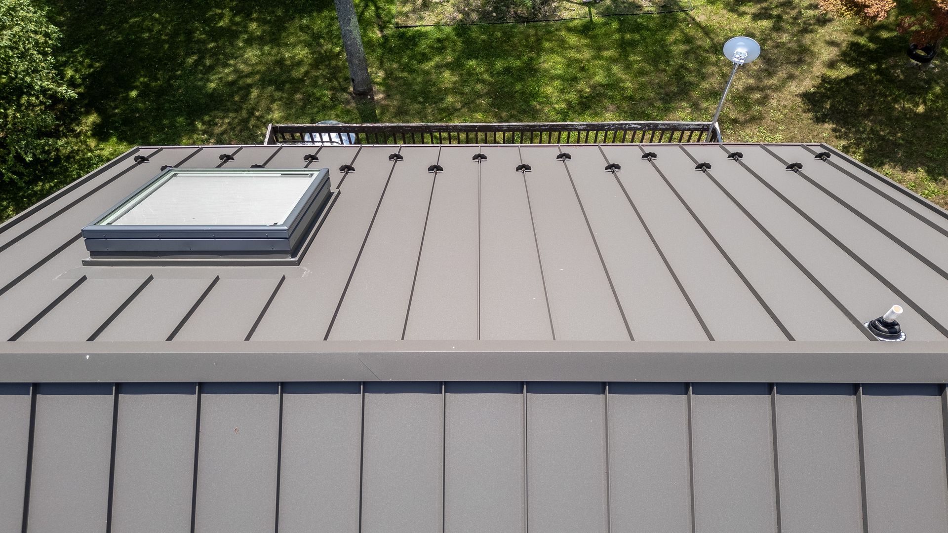 Gray metal roof with skylight, viewed from above, trees in background.