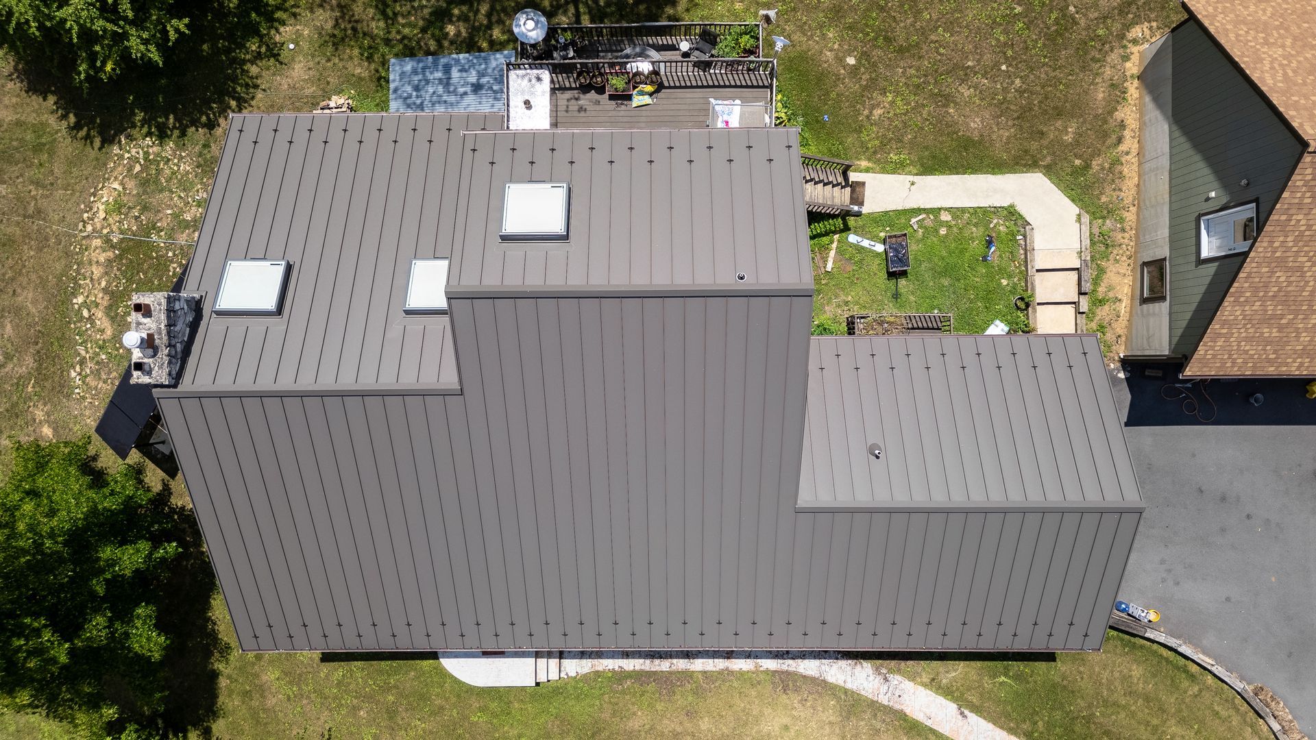 Overhead view of a house with a dark gray metal roof, skylights, and a small yard.