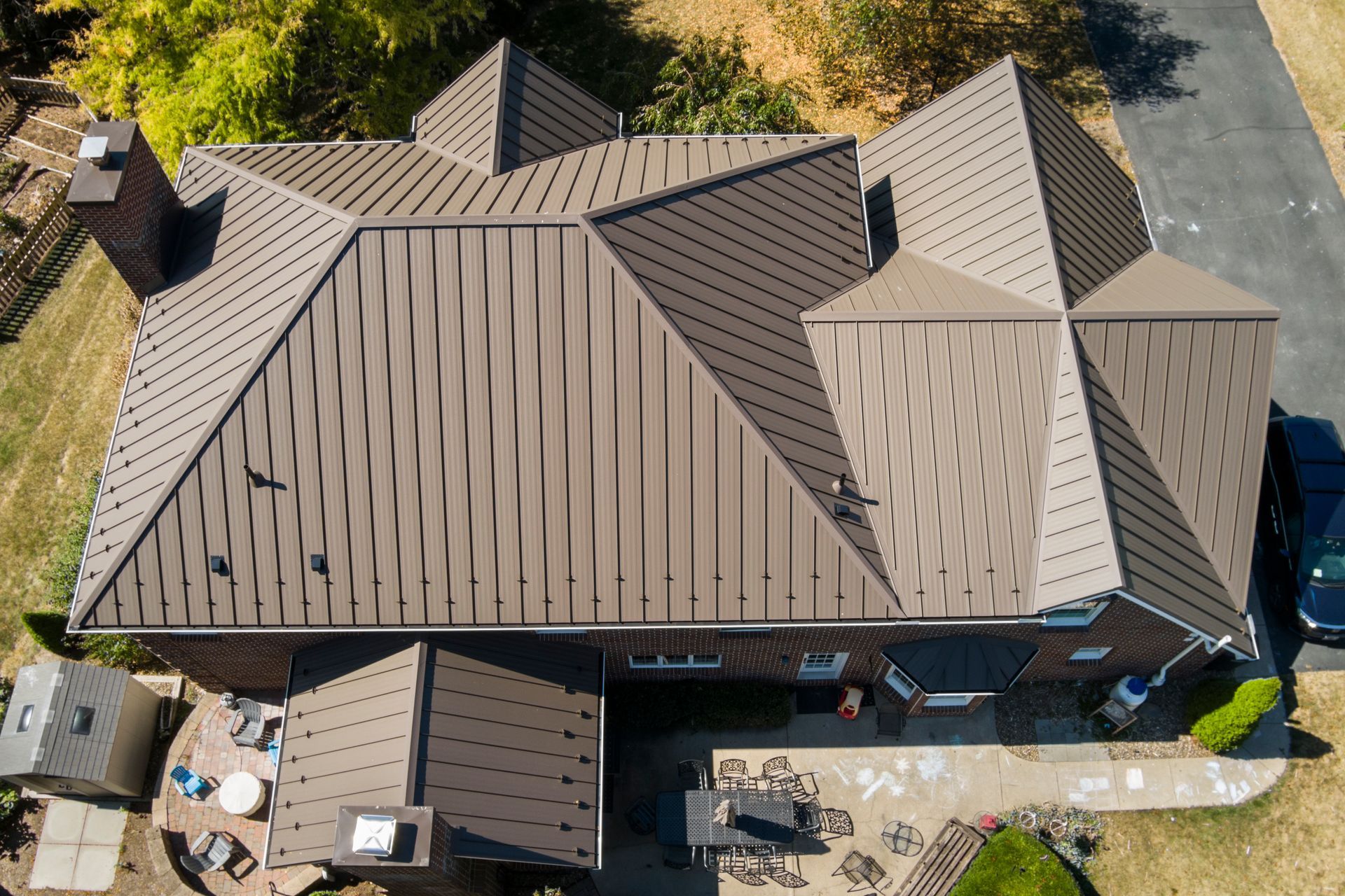 Aerial view of a residential house with a dark brown metal roof featuring a distinct patterned texture.