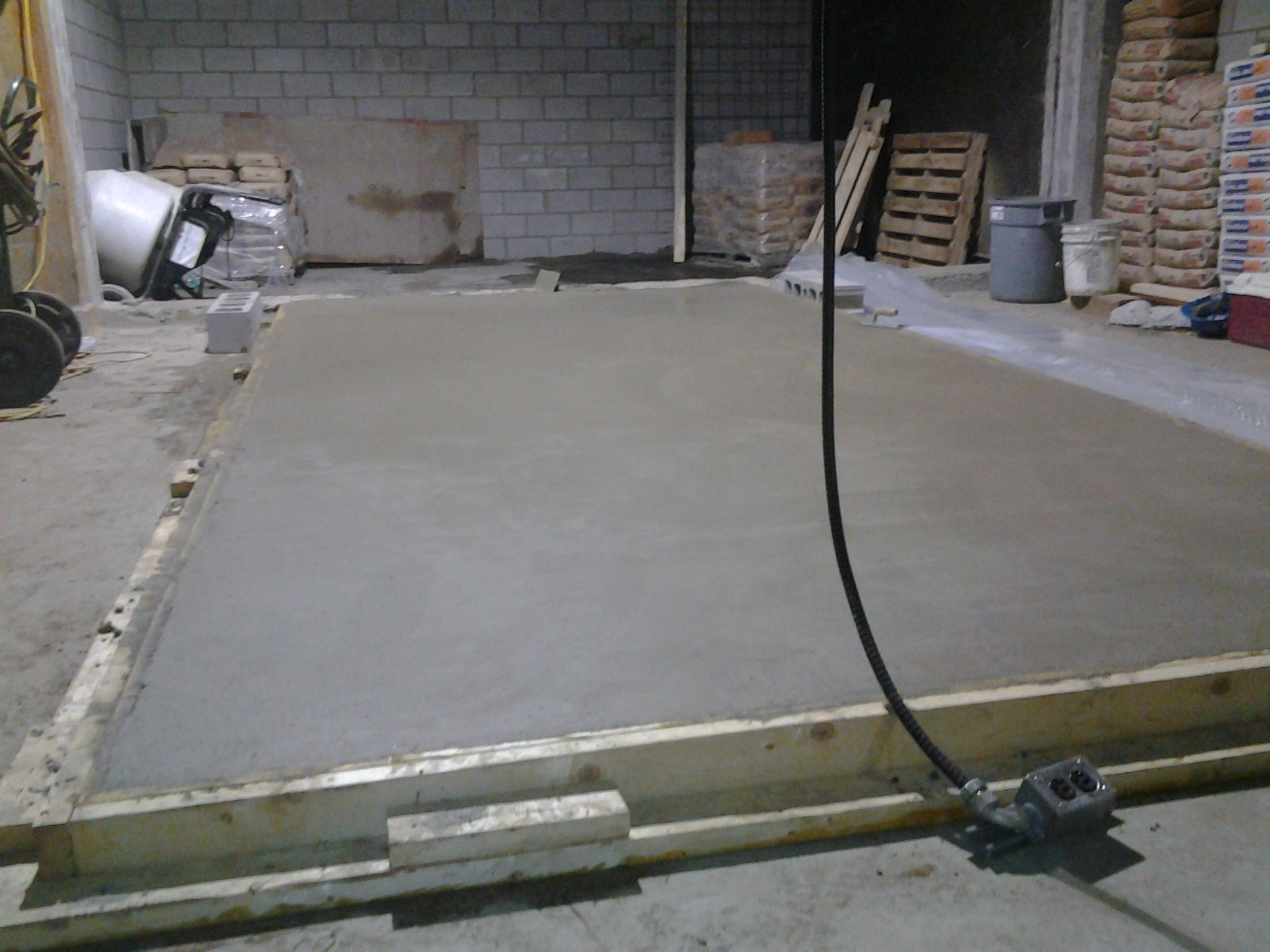 Dalle de béton fraîchement coulée dans une ossature en bois, dans un entrepôt.