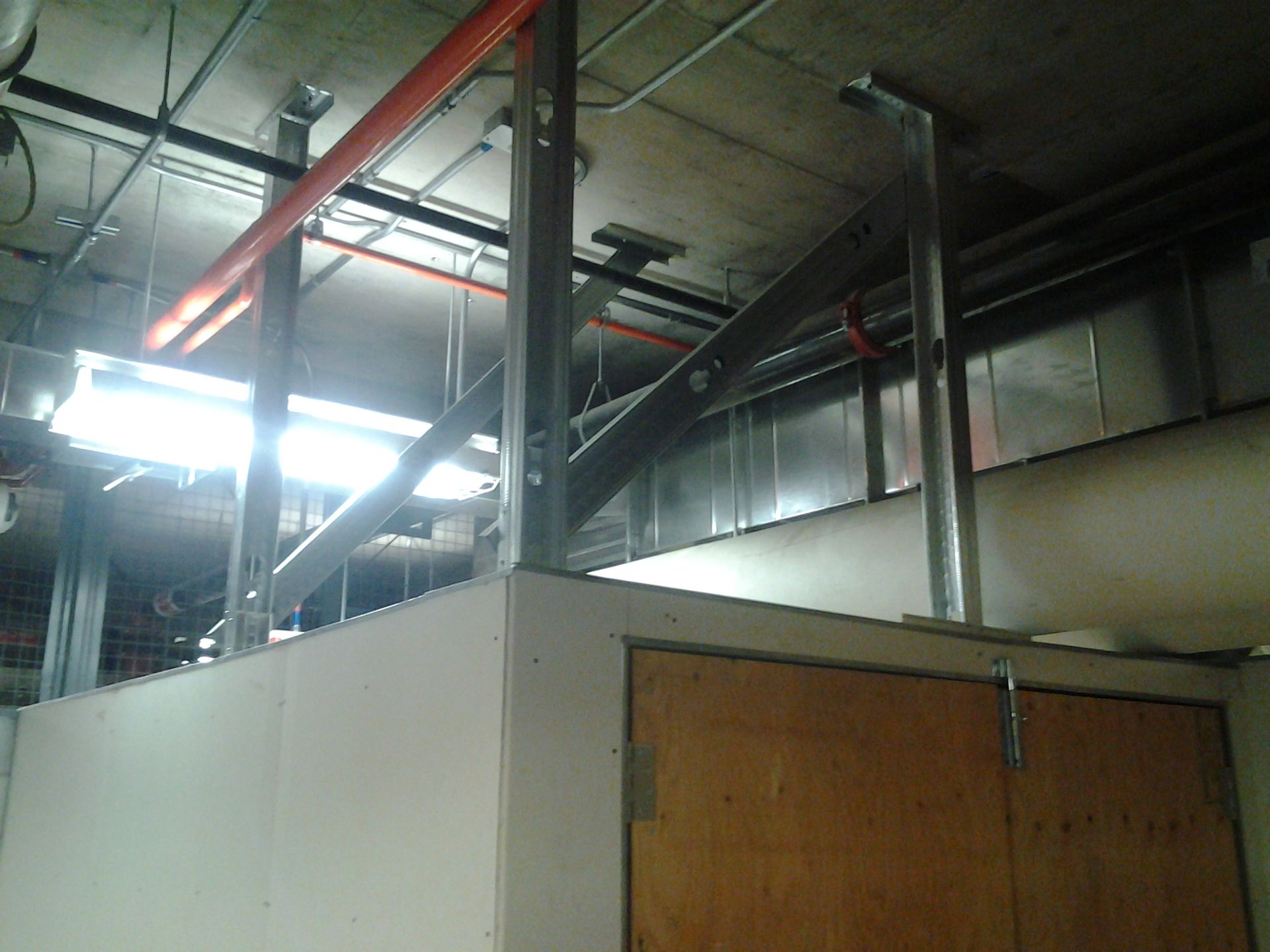 Vue intérieure d'un chantier inachevé ; ossature métallique d'un mur recouvert de plaques de plâtre et porte en bois.