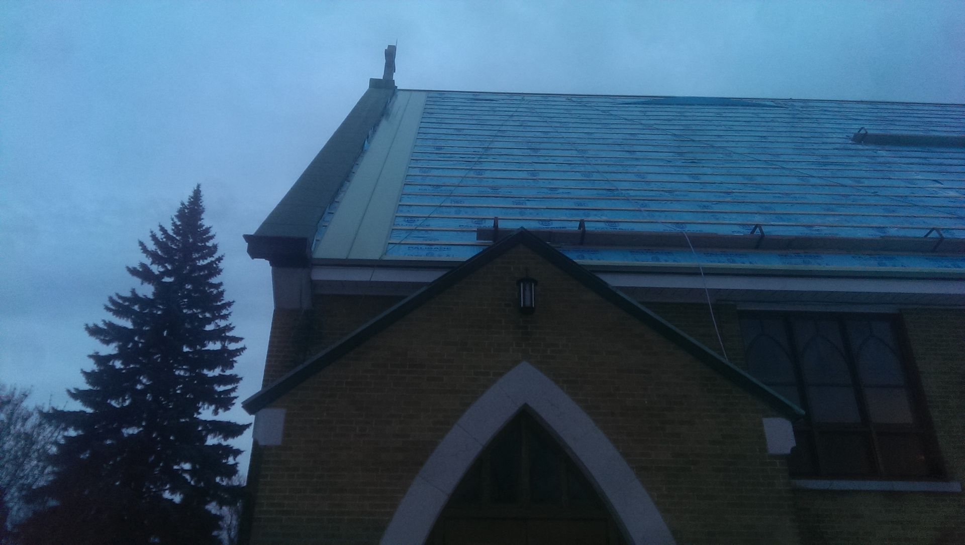 Église de briques au toit sombre sous un ciel nuageux. Une statue orne le toit.