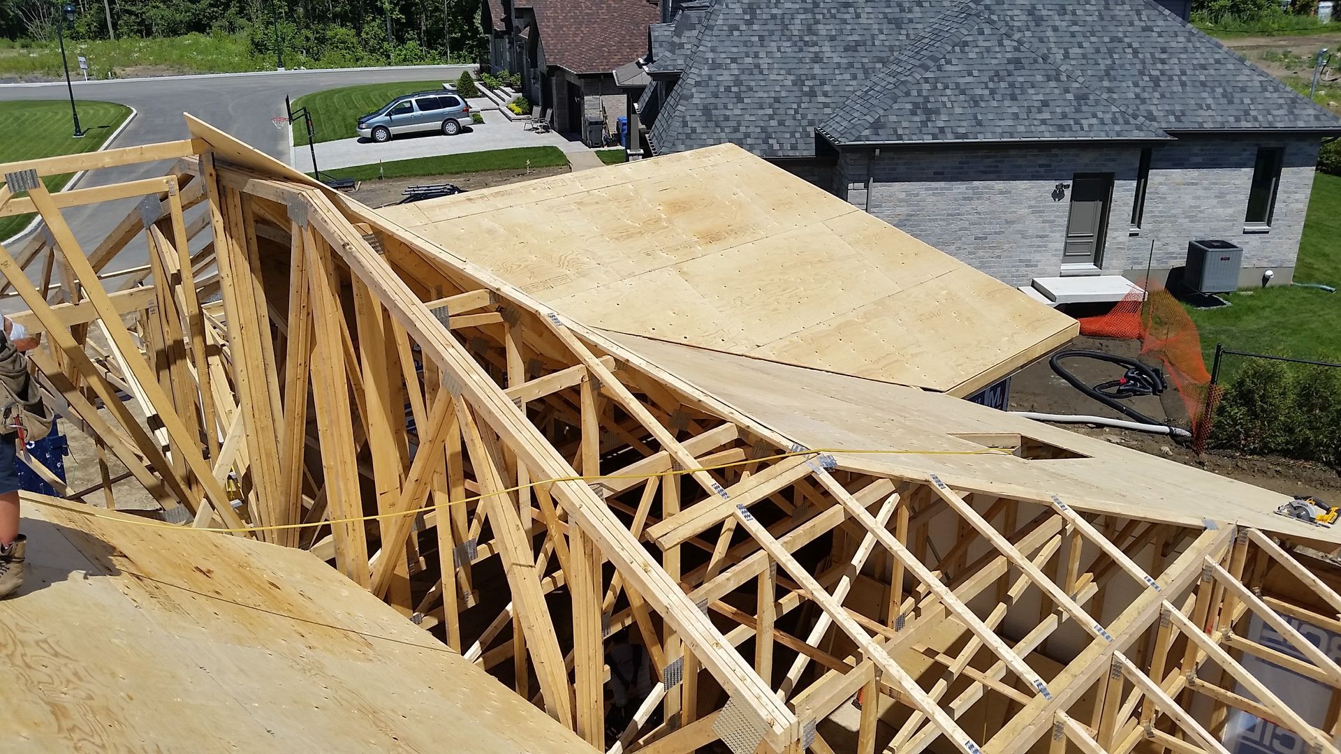 Des fermes de toit en bois sont en cours de construction sur une maison en construction ; le platelage en contreplaqué est partiellement installé.