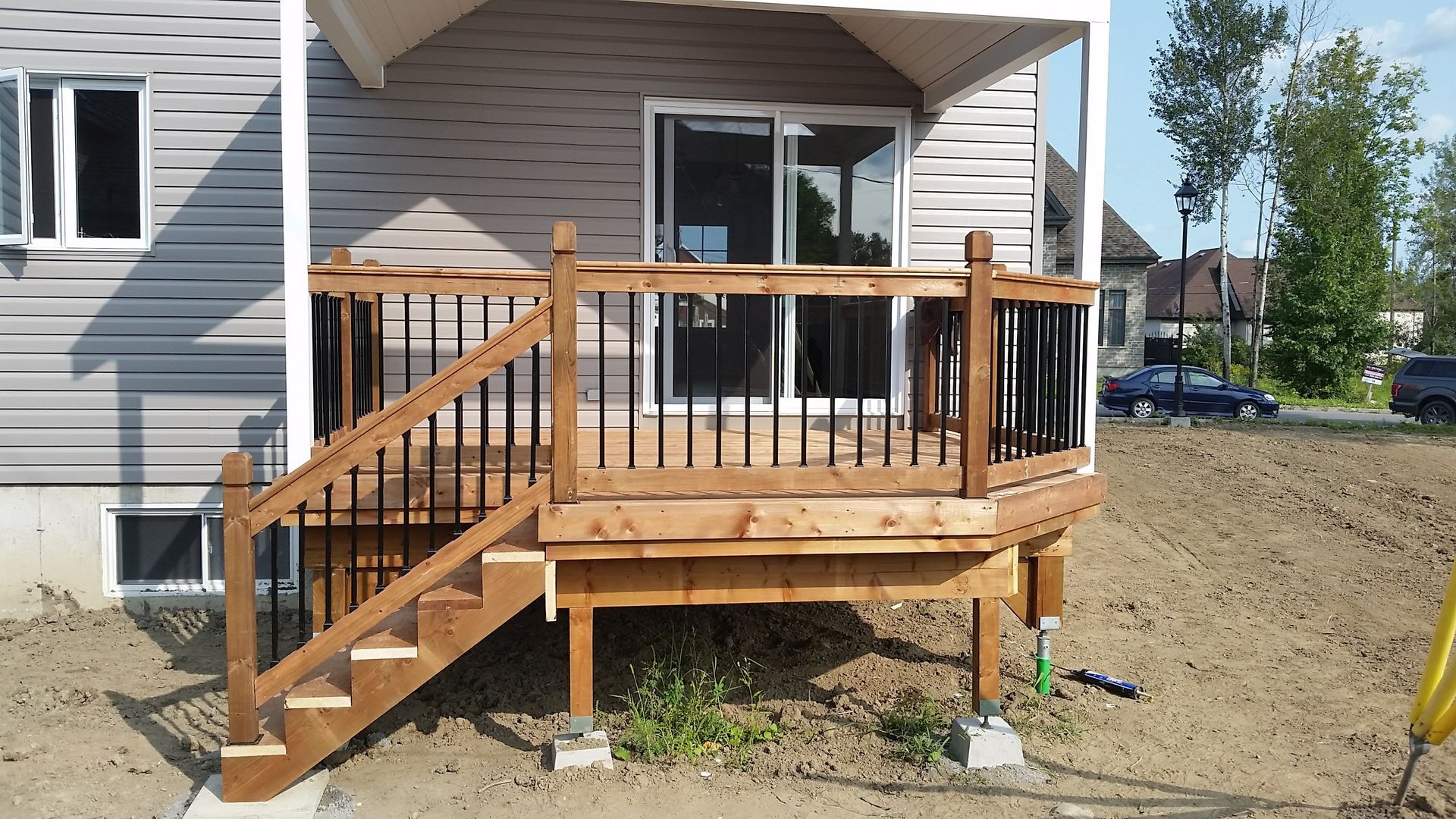 Terrasse en bois avec escalier, rambarde noire et porte coulissante en verre sur une maison.