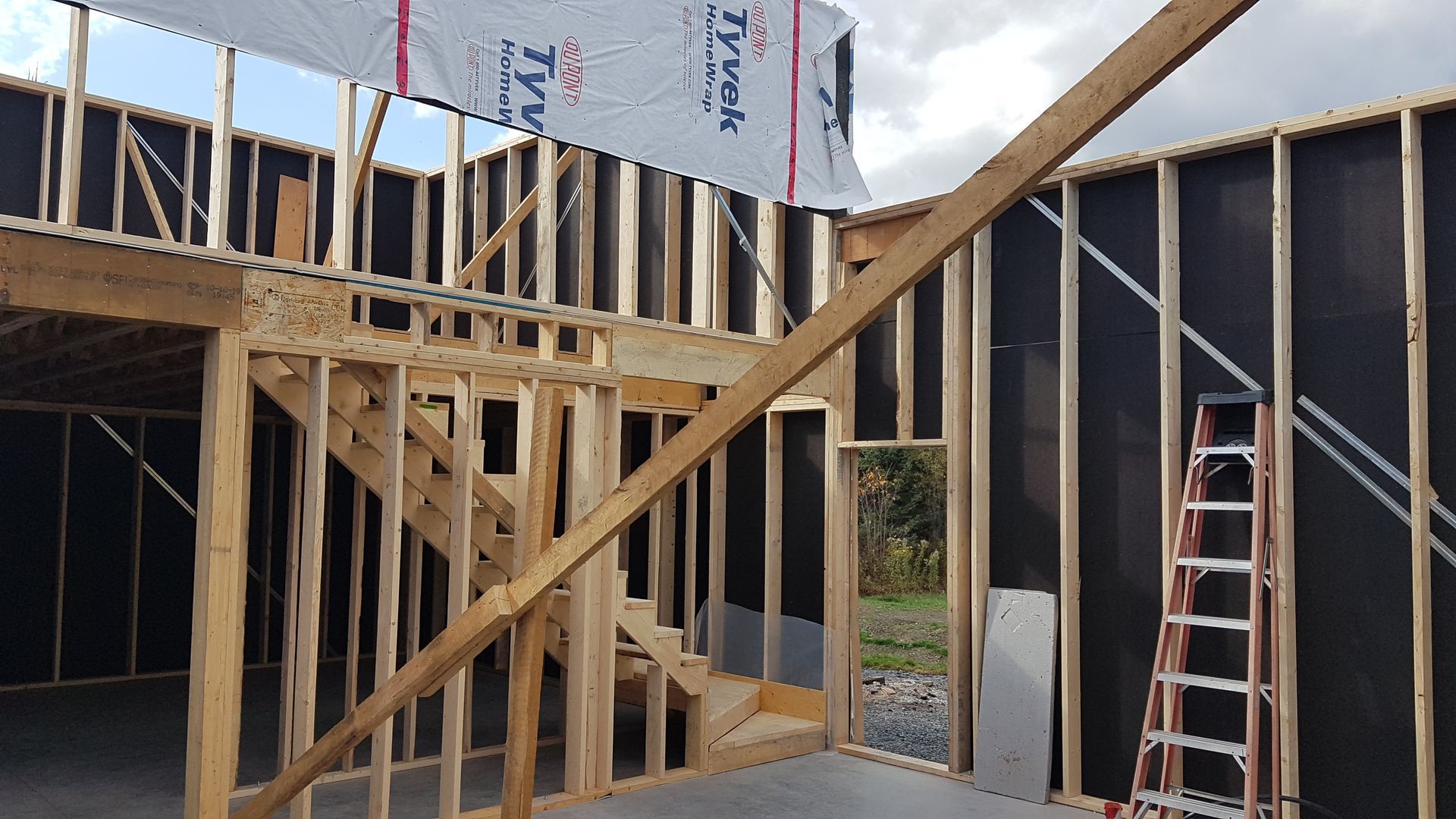 Intérieur d'un bâtiment en construction, montrant la charpente en bois, un escalier et une échelle.