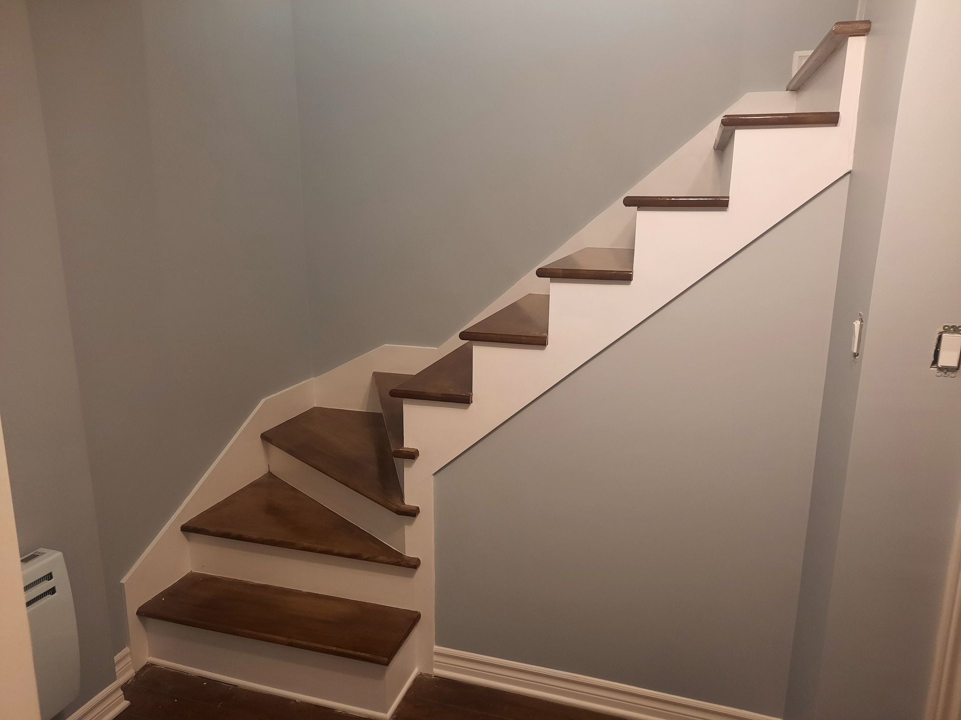 Escalier avec marches marron, contremarches blanches et murs gris.