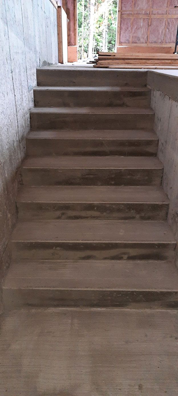 Un escalier en béton mène à une ouverture laissant apparaître de la verdure.