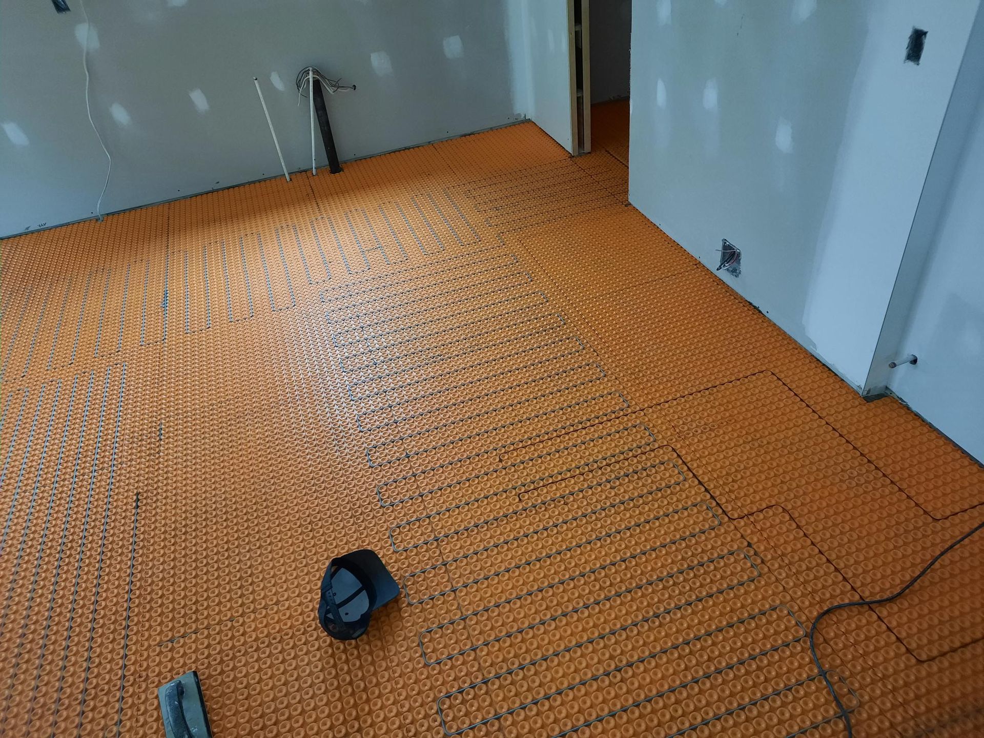 Système de chauffage au sol radiant orange installé sur le sol d'une pièce en construction.