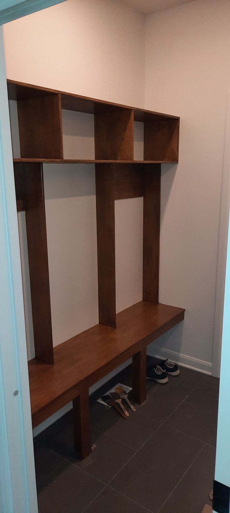 Banquette en bois intégrée avec étagères dans une pièce, sol carrelé marron, murs blancs.