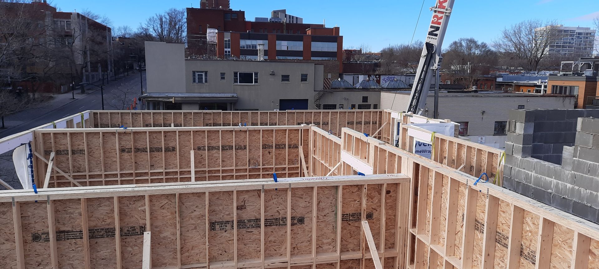 Chantier de construction avec charpente en bois, grue et bâtiments sous un ciel bleu.